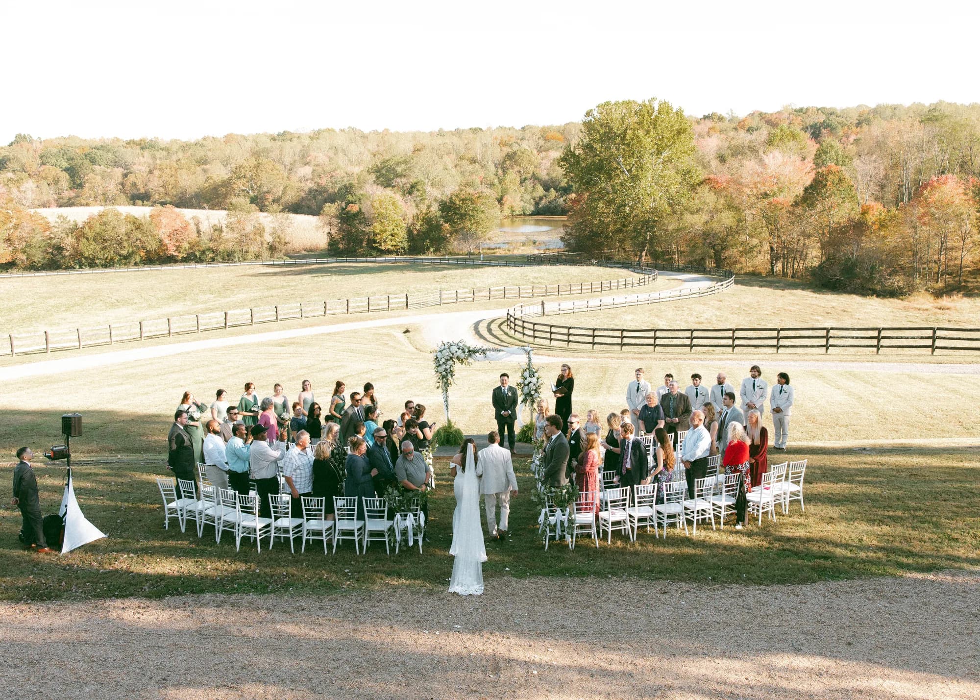 Aerial view of outdoor wedding ceremony on Rixey Manor grounds with guests seated in semicircle, fall foliage backdrop