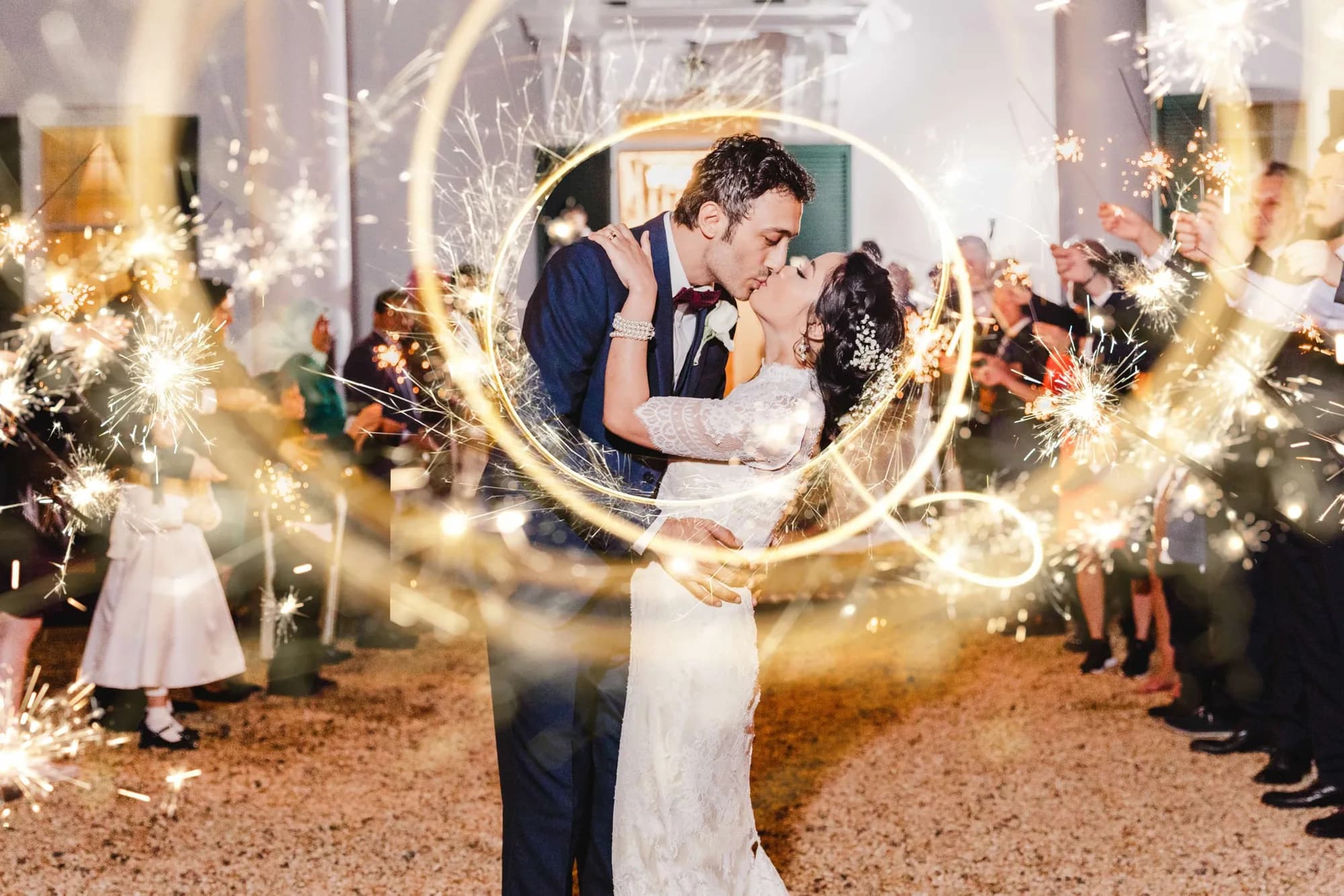 Bride and groom share a kiss surrounded by swirling sparklers and cheering guests during grand exit