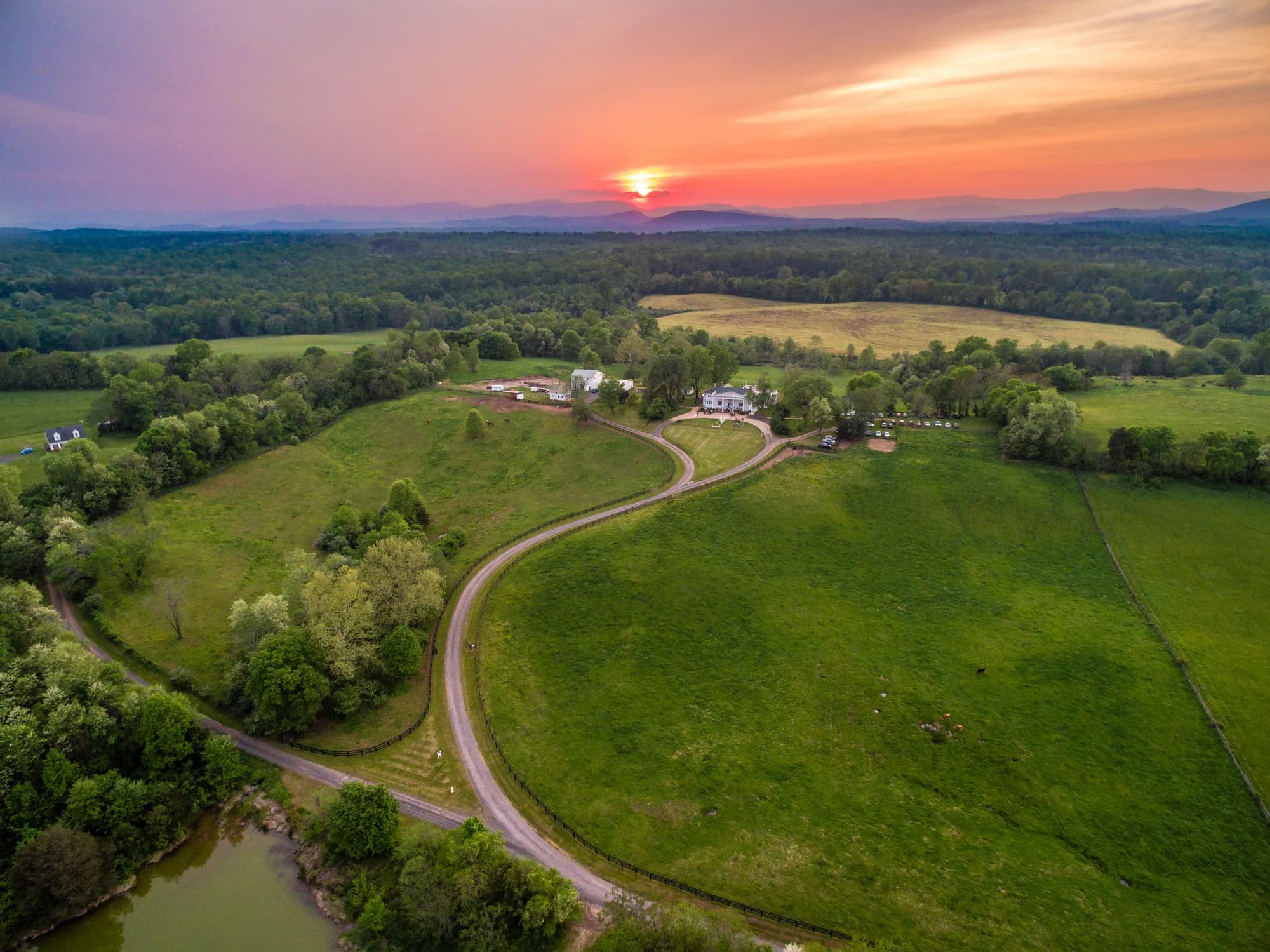 Aerial sunset view of Rixey Manor estate with winding drive, green fields, and Blue Ridge Mountains backdrop