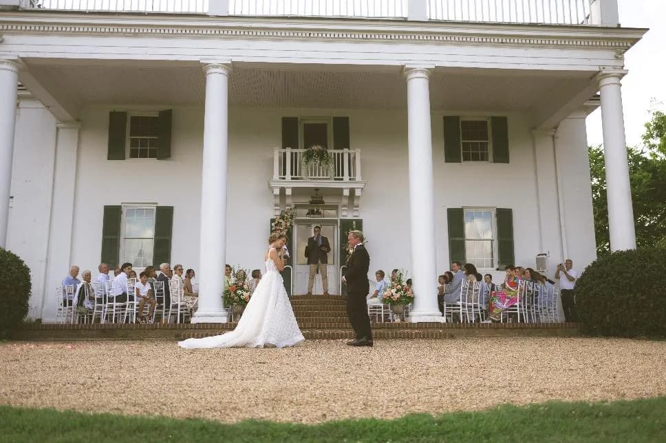 Bride and groom face each other during outdoor ceremony on the grand lawn at Rixey Manor's white columned estate