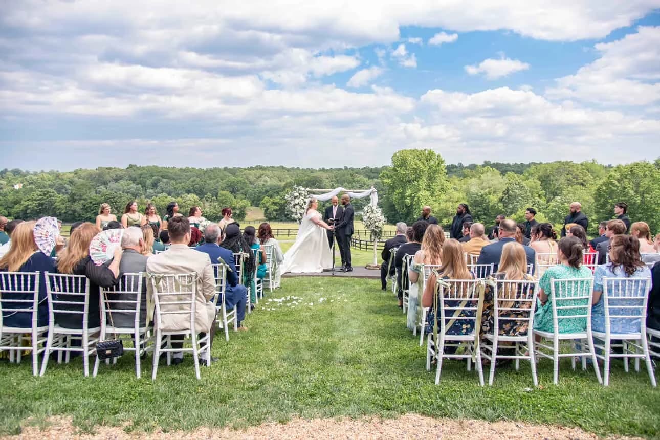 Outdoor wedding ceremony at Rixey Manor with guests seated on lush green lawn beneath a floral arch
