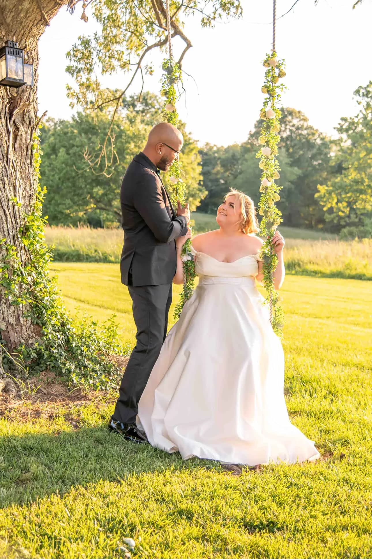 Bride on floral swing gazes at groom in golden hour light among Rixey Manor's lush grounds