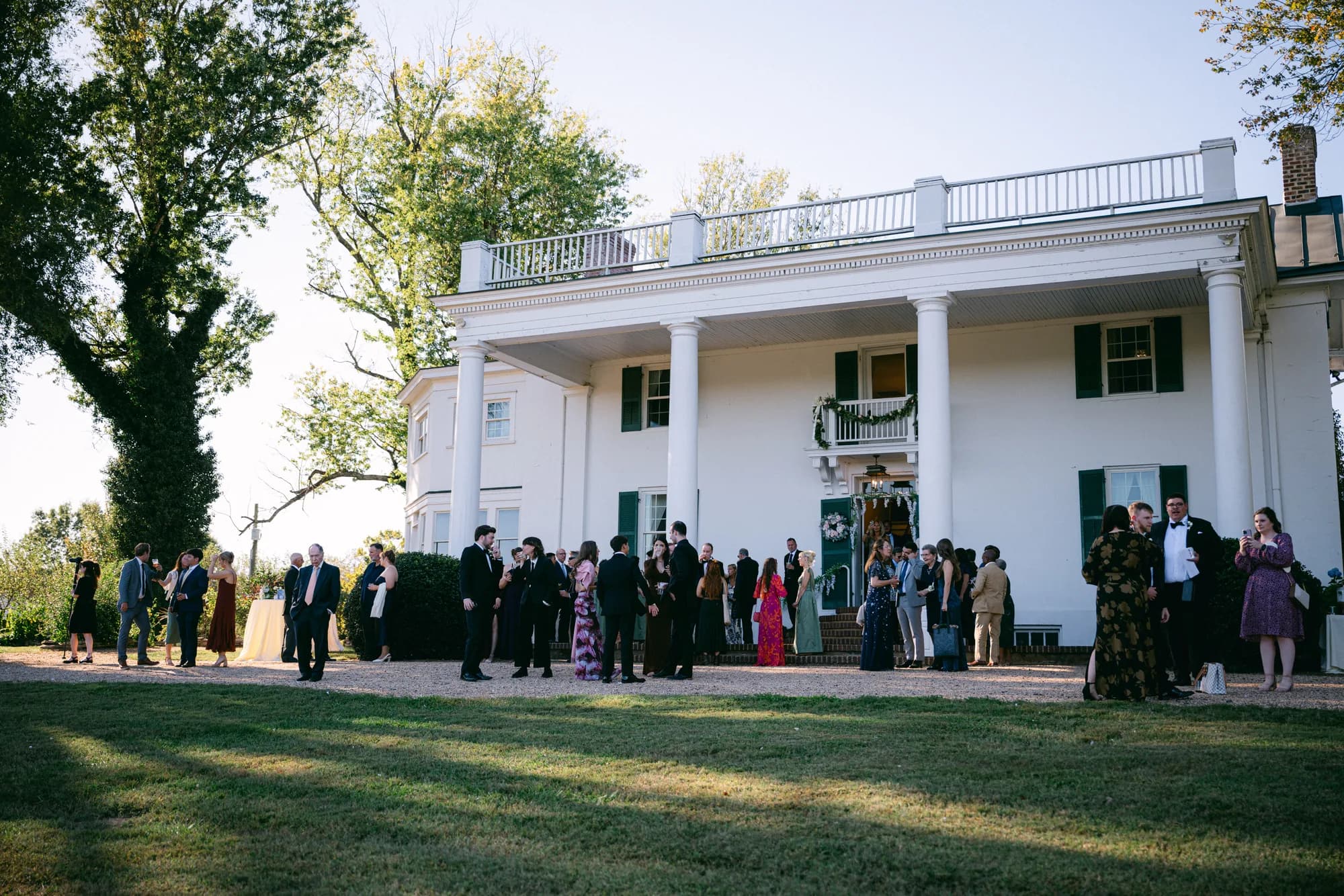 Wedding cocktail hour guests mingling on the lawn outside Rixey Manor's white columned estate facade