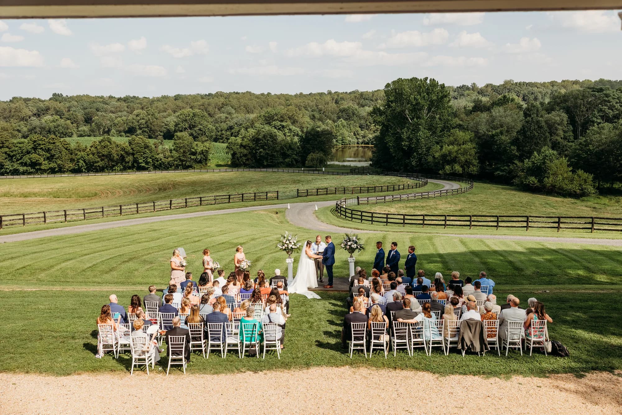 Aerial view of outdoor wedding ceremony on Rixey Manor's sweeping lawn with pond, fenced pastures, and forest backdrop