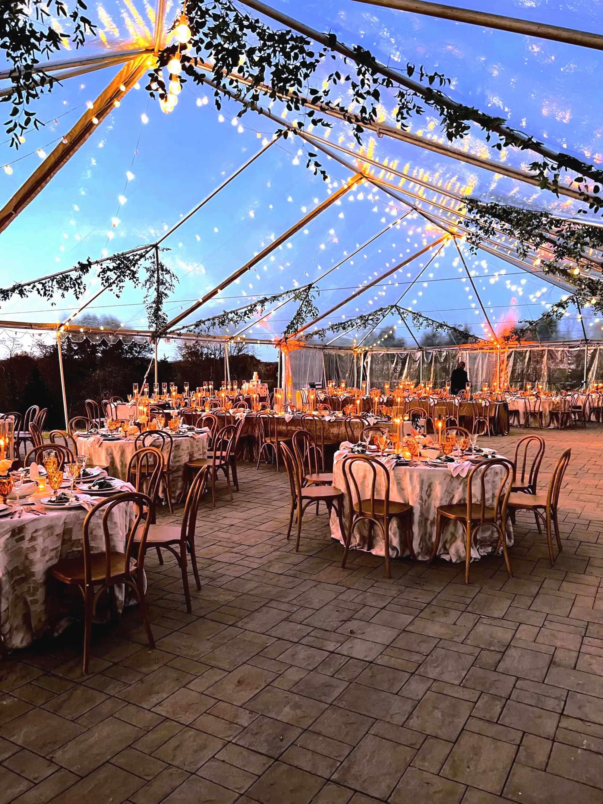 Glowing reception tables under a clear tent at dusk at Rixey Manor, with string lights and candlelit centerpieces