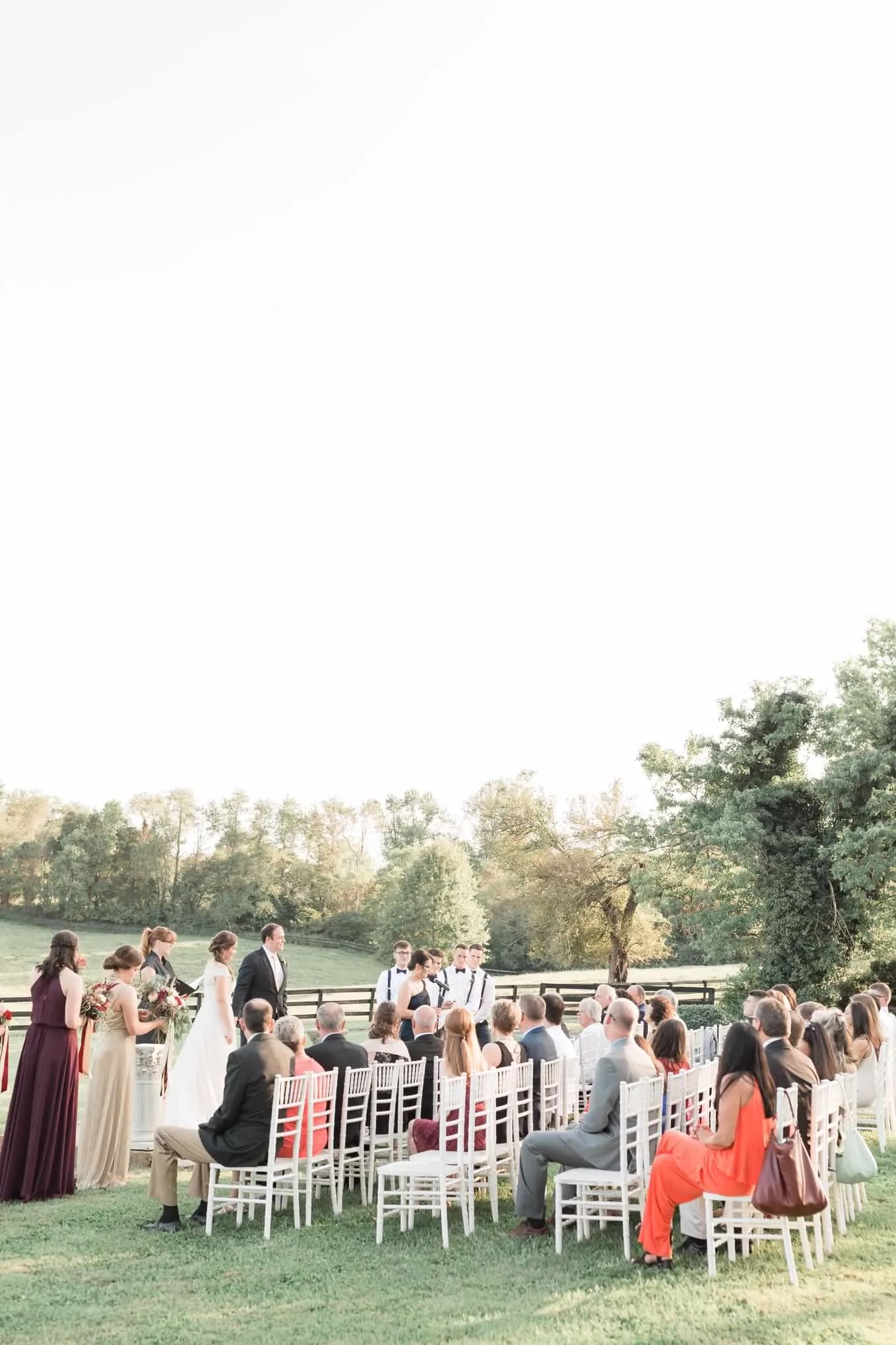 Outdoor wedding ceremony on Rixey Manor grounds with guests seated in white chairs amid rolling hills and trees
