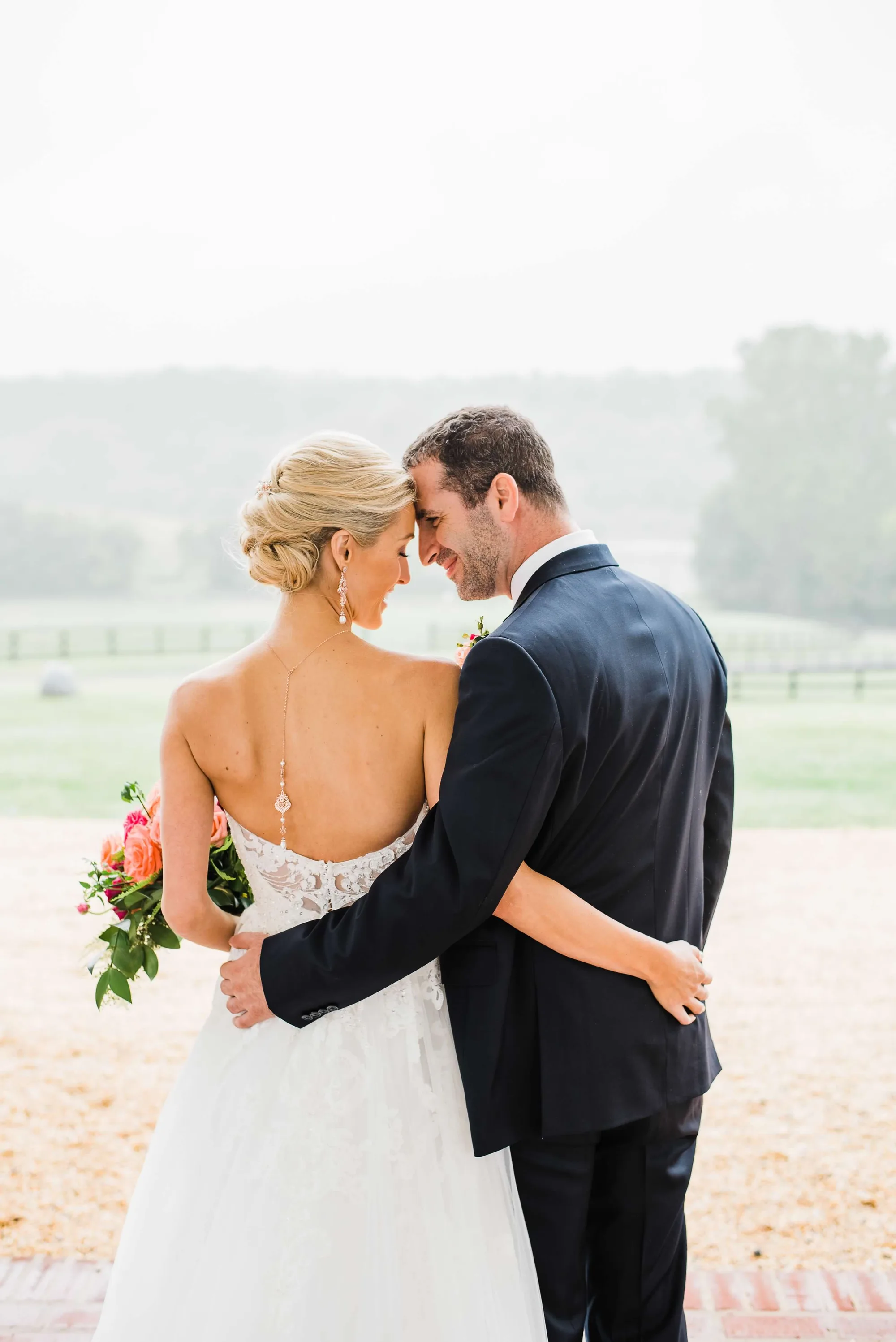 Bride and groom embrace on Rixey Manor terrace, smiling forehead-to-forehead with sweeping pastoral grounds behind them.