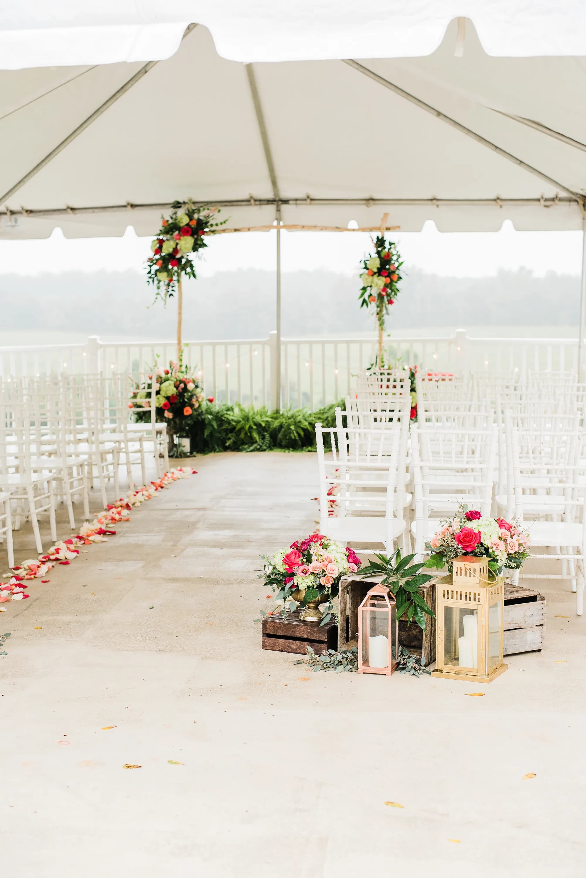 Floral-decorated ceremony aisle under tent at Rixey Manor with rose petals, lanterns, and wooden crates overlooking green hills