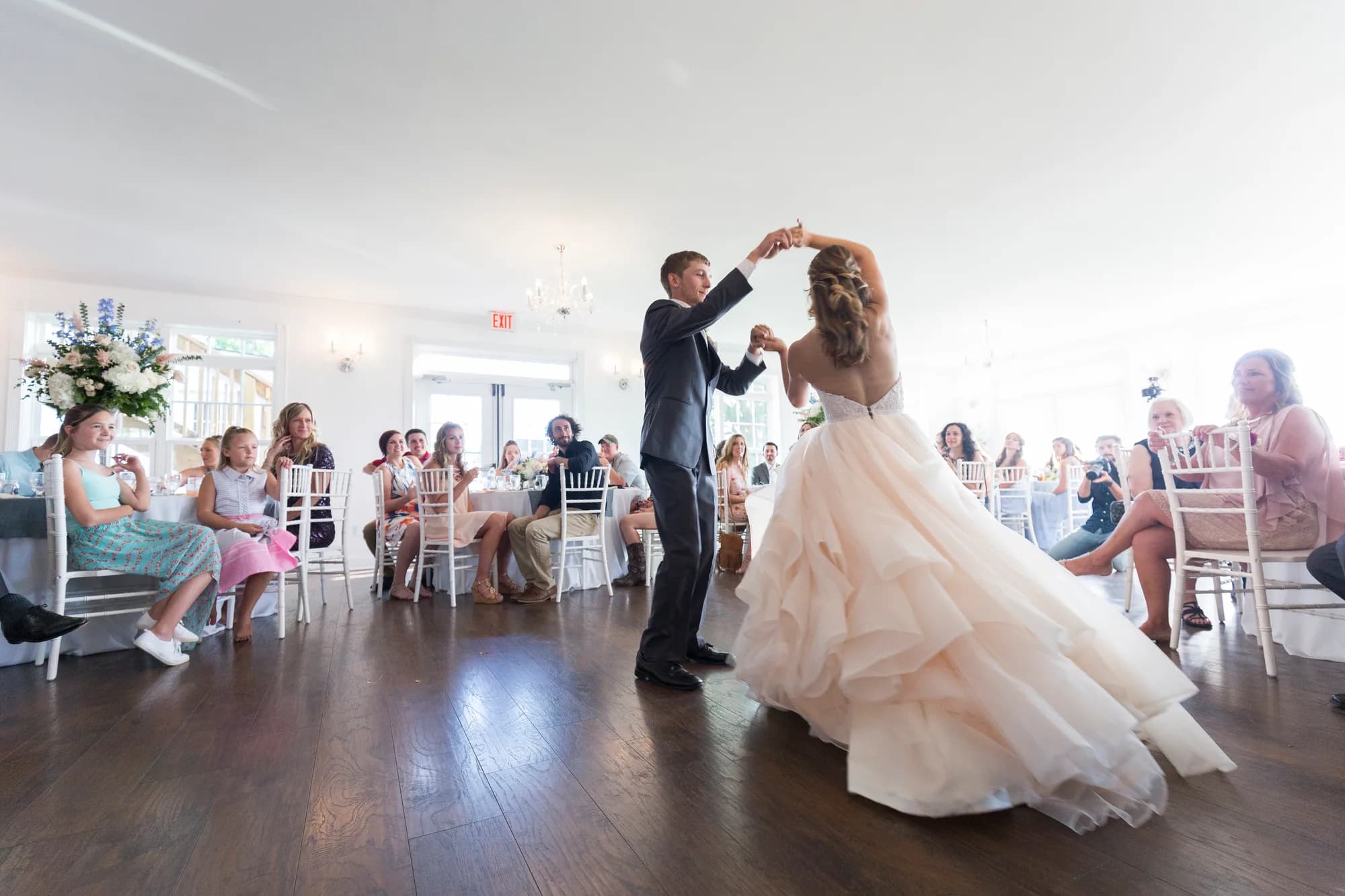 Bride and groom share first dance in bright Rixey Manor ballroom as guests look on