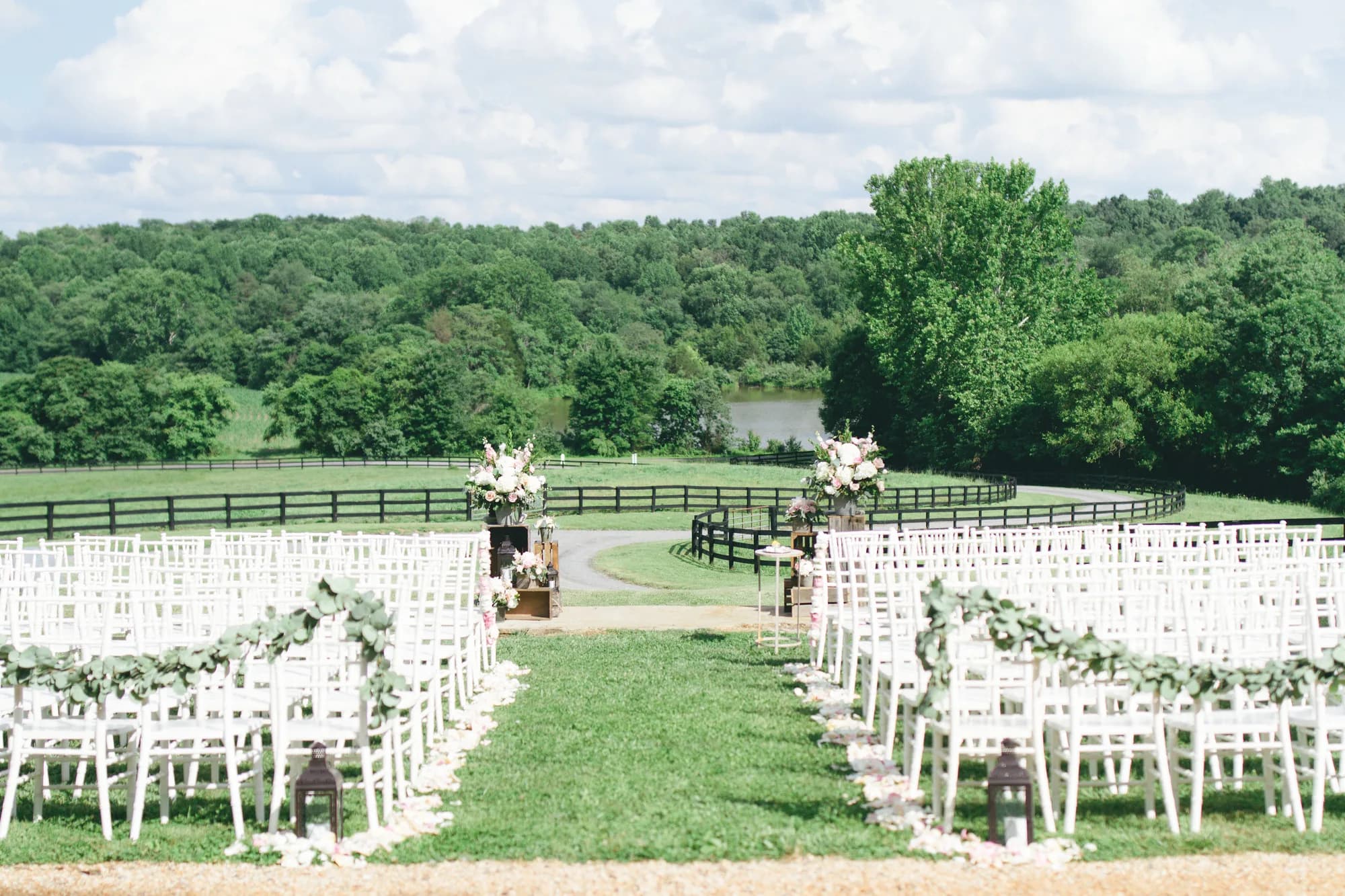 Sun-lit outdoor ceremony setup at Rixey Manor with white chairs, floral aisle, black fencing, and lush Virginia countryside backdrop