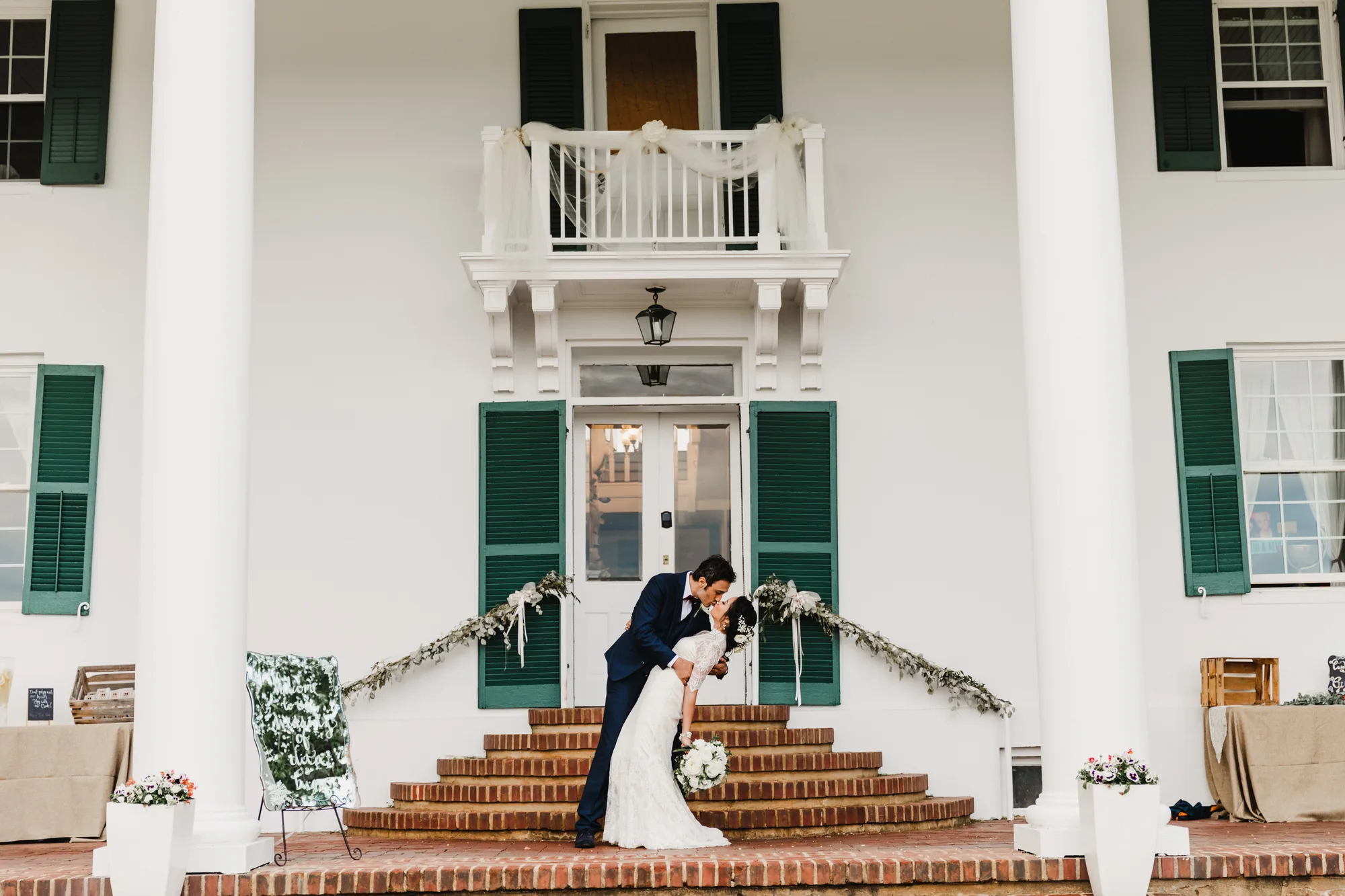 Couple shares a romantic dip kiss on the brick carriage steps of Rixey Manor's white-columned front portico