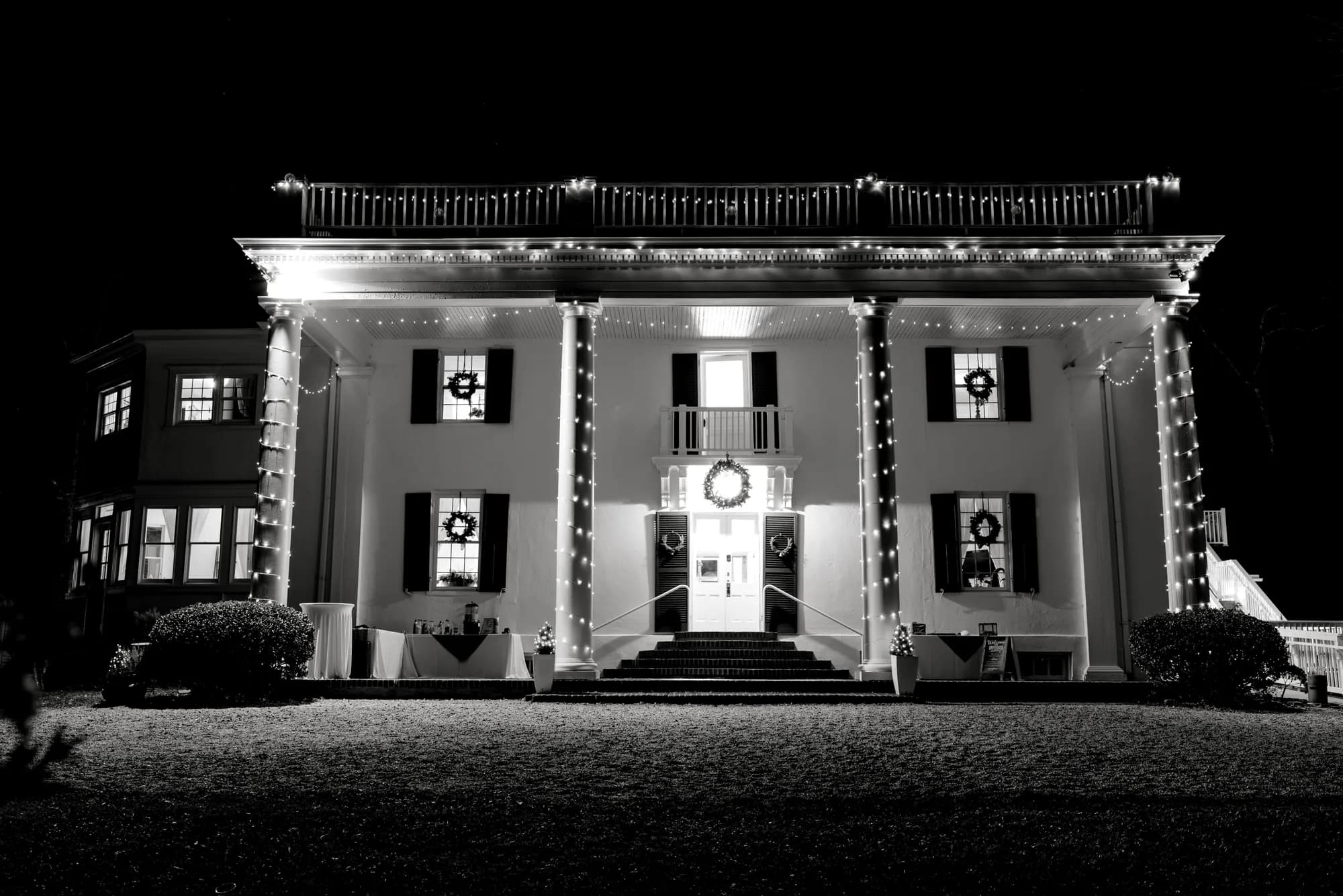 Rixey Manor estate lit with holiday lights and wreaths at night, black and white exterior facade