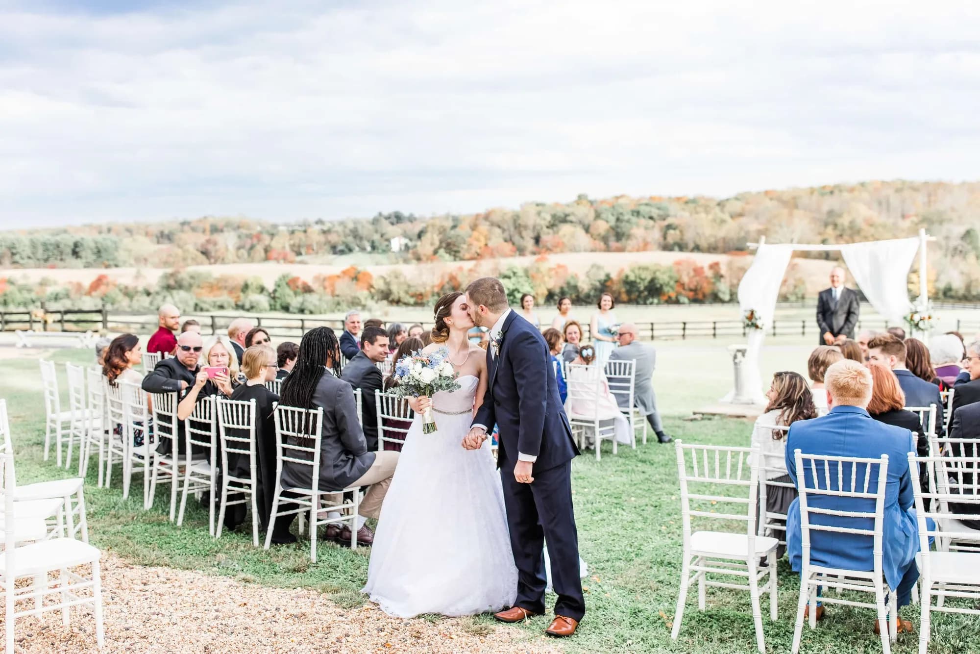Bride and groom share a kiss at the end of the aisle at Rixey Manor's outdoor ceremony amid fall foliage