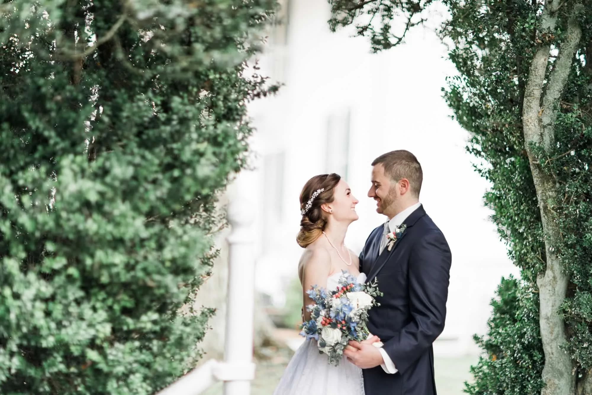 Bride and groom share a tender moment framed by lush hedges and white columns at Rixey Manor.