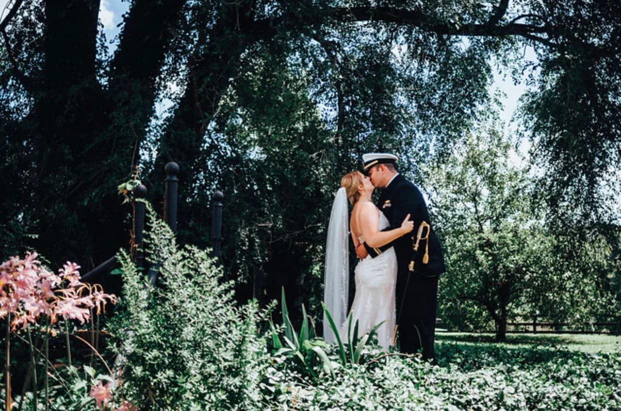 Military groom and bride share a kiss amid lush garden greenery at Rixey Manor estate grounds