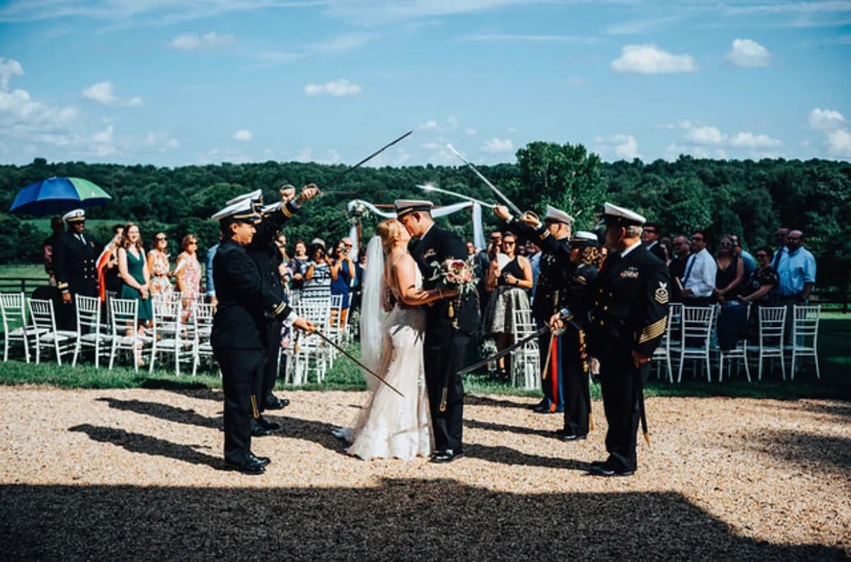 Military sword arch as bride and groom kiss at outdoor Rixey Manor ceremony under blue summer skies
