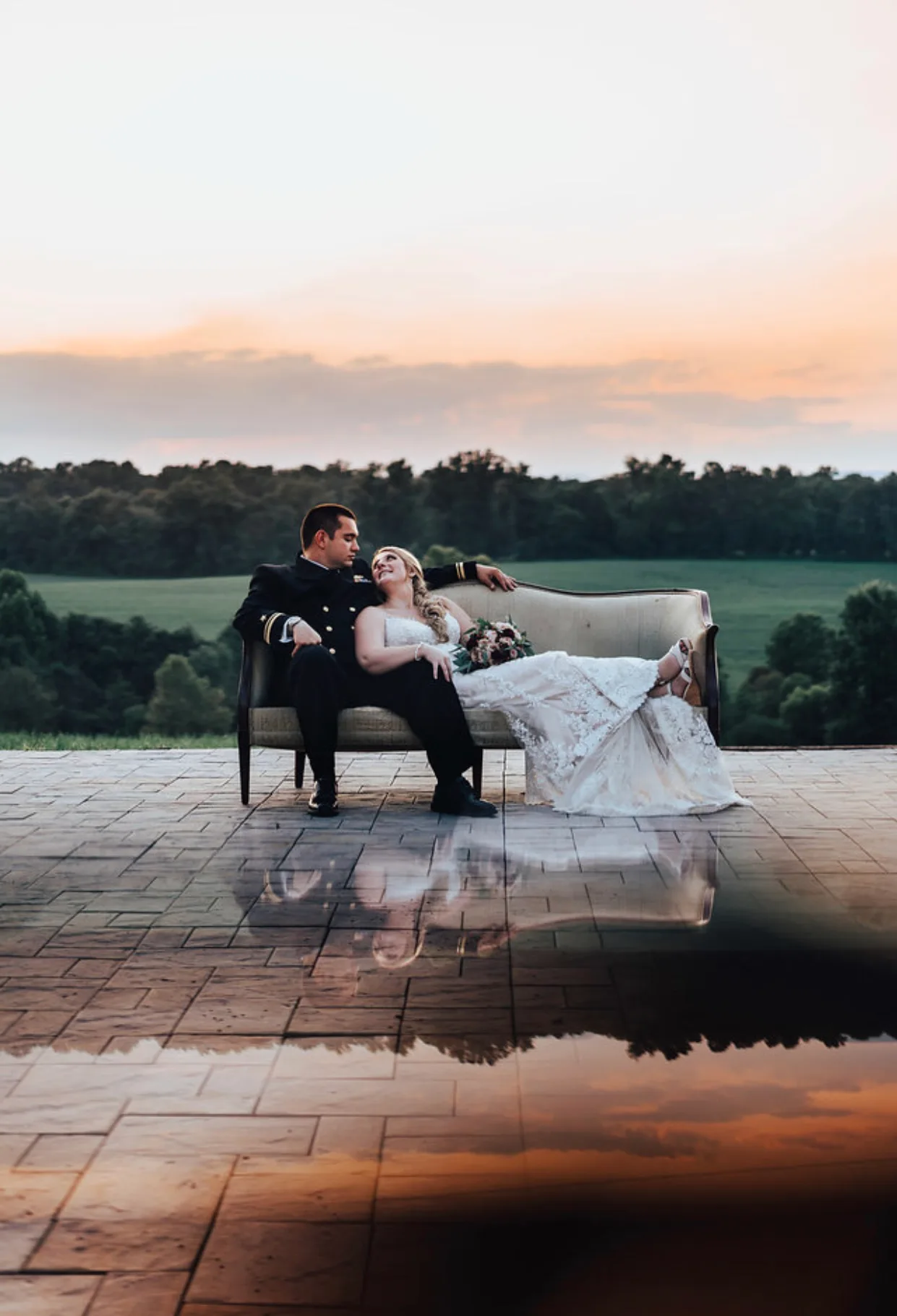 Bride and groom on vintage sofa at Rixey Manor terrace at sunset, reflected in pooled water below