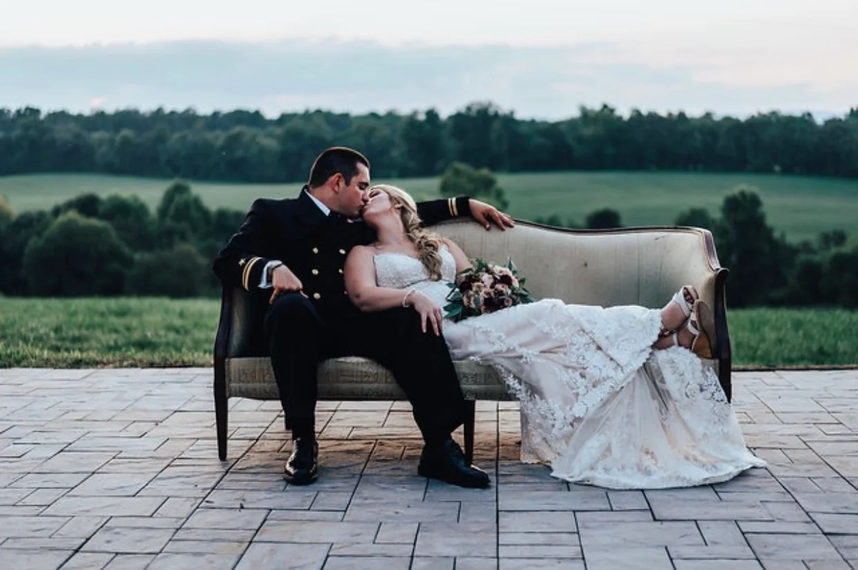 Bride and groom share a kiss on a vintage sofa on Rixey Manor's terrace overlooking rolling Virginia countryside