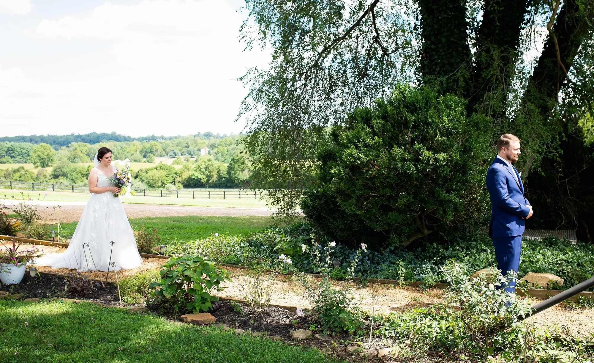 Bride approaches groom from behind during first look in Rixey Manor garden with rolling Virginia countryside beyond
