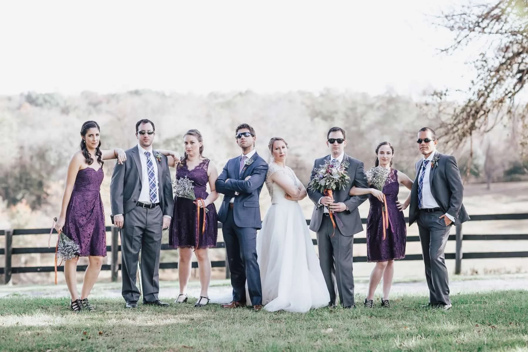 Wedding party poses dramatically in sunglasses on Rixey Manor grounds with rustic fence and rolling hills behind