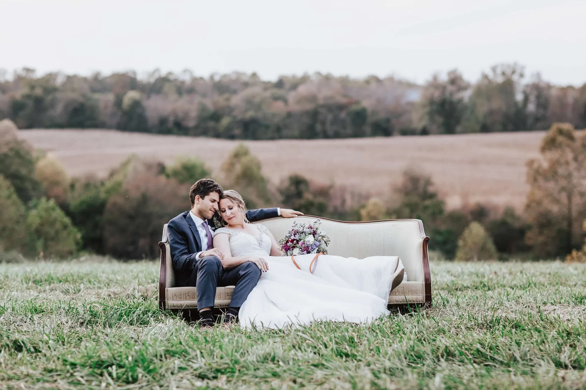 Bride and groom embracing on a vintage sofa in a pastoral Virginia field with rolling hills behind them