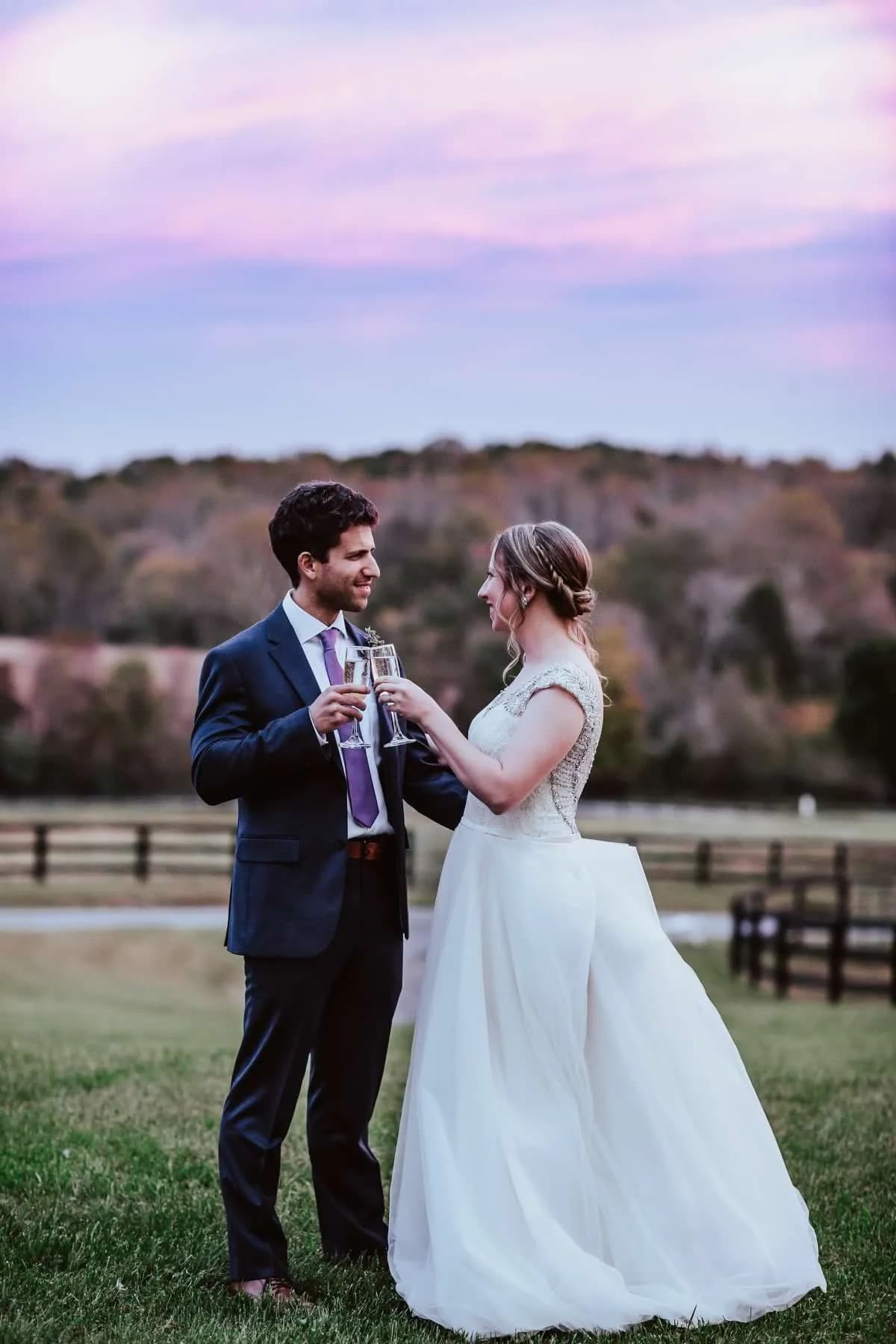 Bride and groom toast with champagne at sunset on Rixey Manor's pastoral grounds under a violet sky