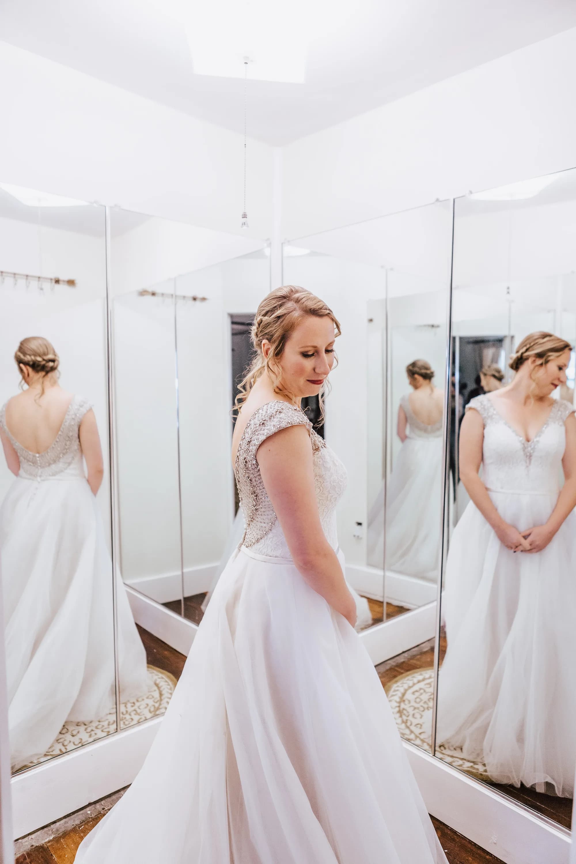 Bride in beaded cap-sleeve gown poses in triple mirror bridal suite, reflecting multiple elegant angles