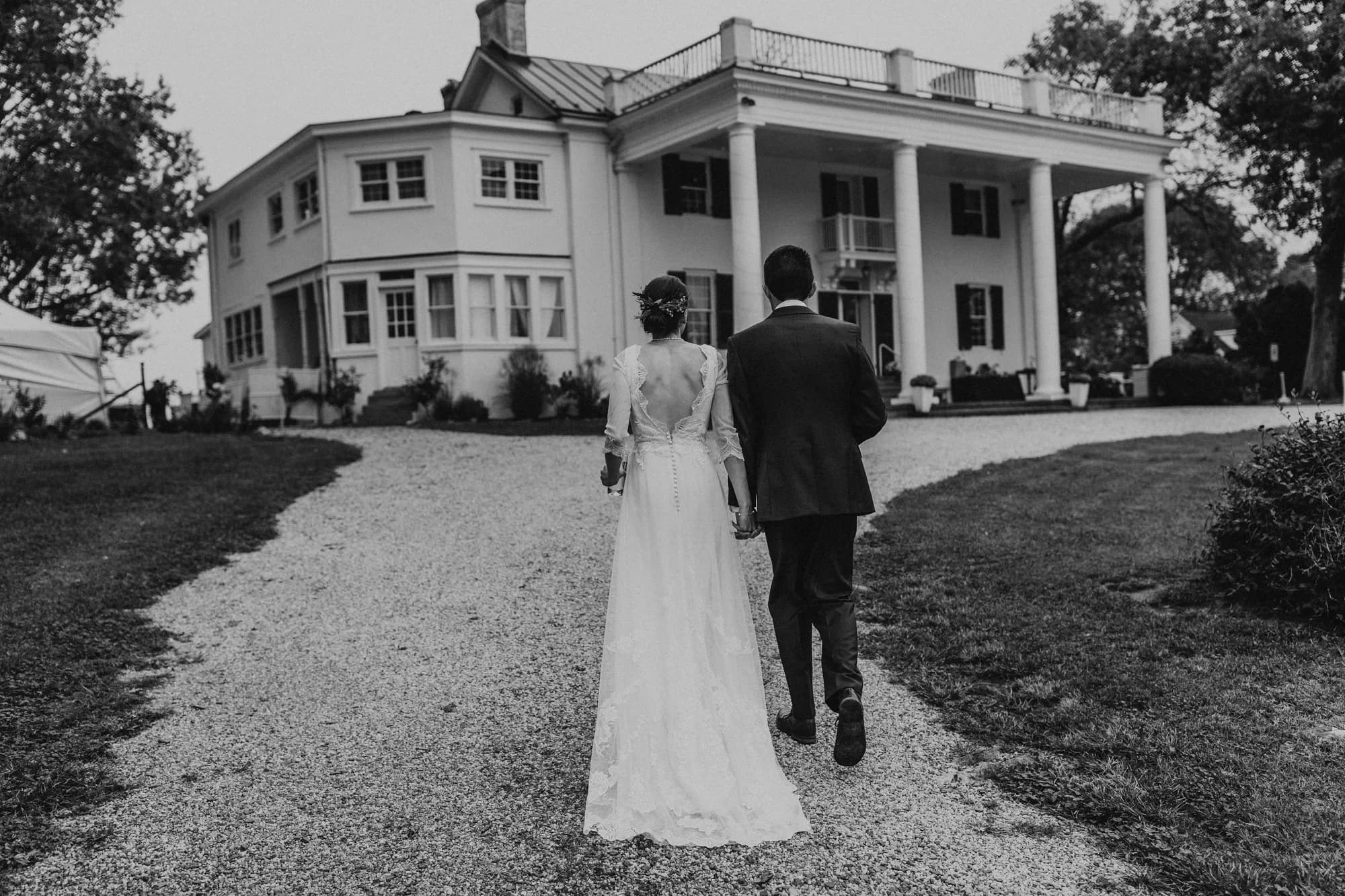 Bride and groom walk hand-in-hand toward Rixey Manor's columned facade along a gravel path