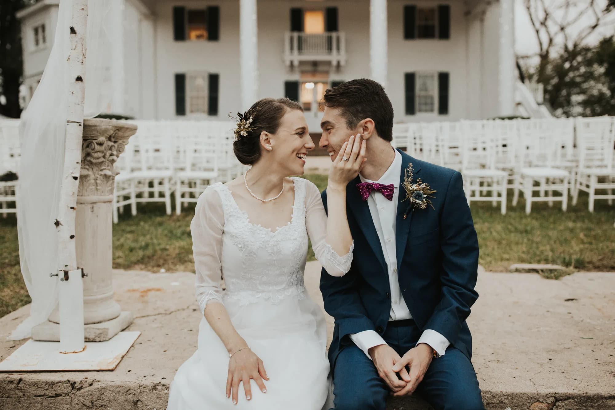 Bride and groom share a tender laugh outside Rixey Manor's white columned facade with ceremony chairs behind them