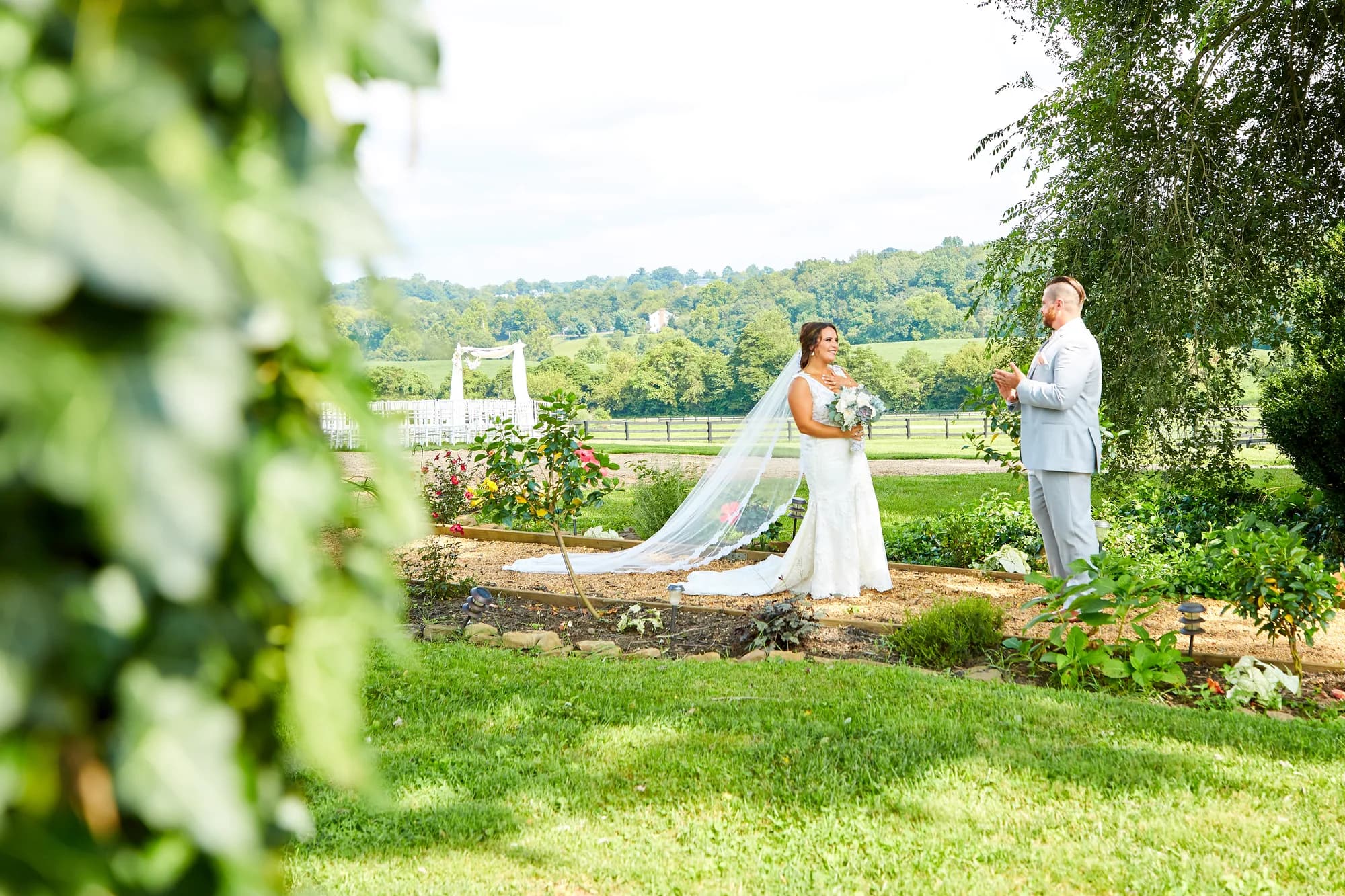 Bride and groom share a first look moment in Rixey Manor's lush garden with rolling Virginia hills behind them.