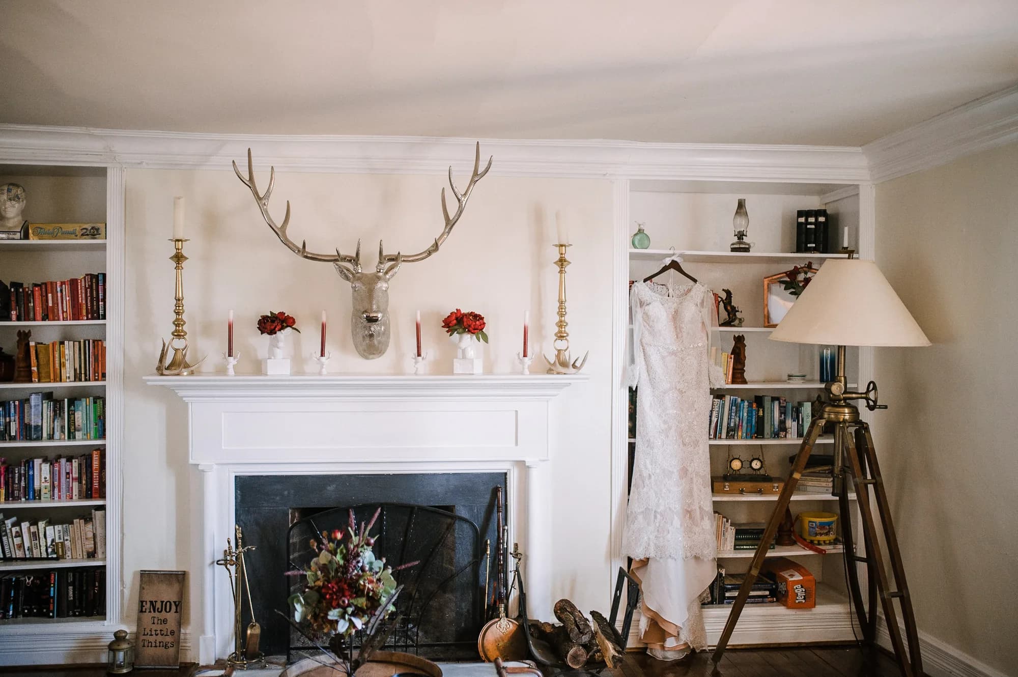Wedding dress hanging near fireplace mantel with deer mount, candles, and built-in bookshelves at Rixey Manor