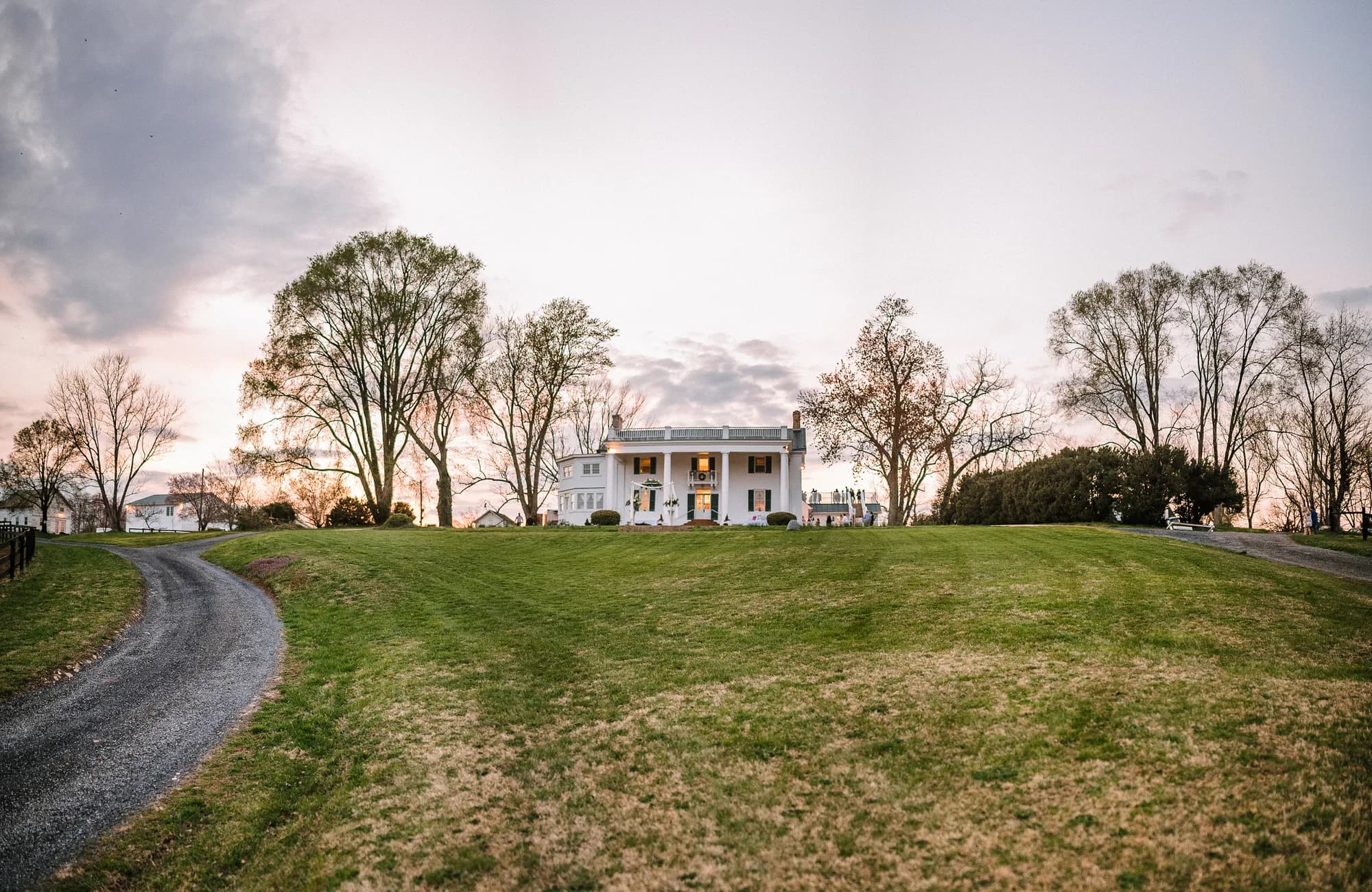 White antebellum manor atop a rolling green hill at dusk, framed by bare trees at Rixey Manor, Virginia