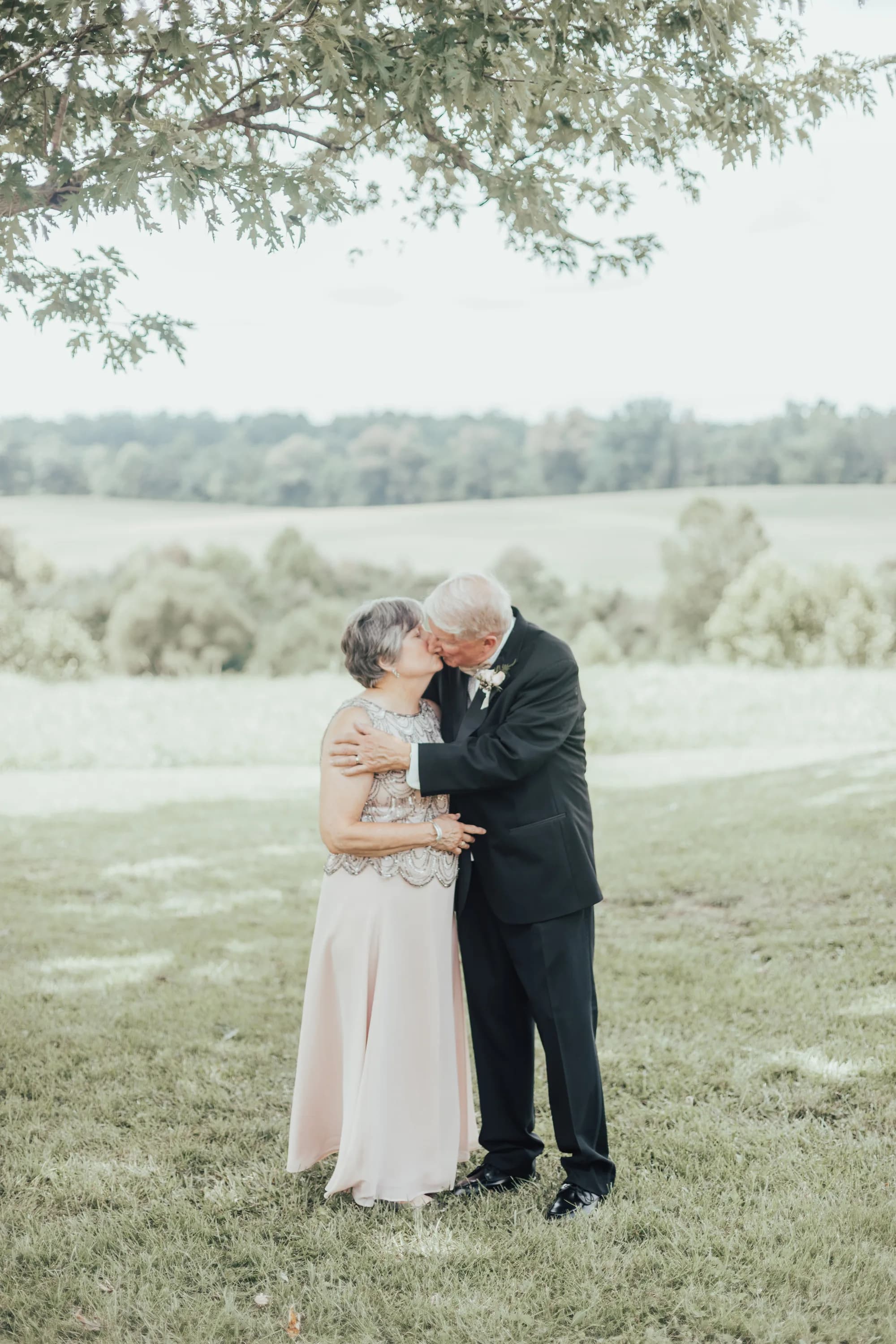 Elderly couple sharing a tender kiss outdoors on lush green grounds during a wedding celebration