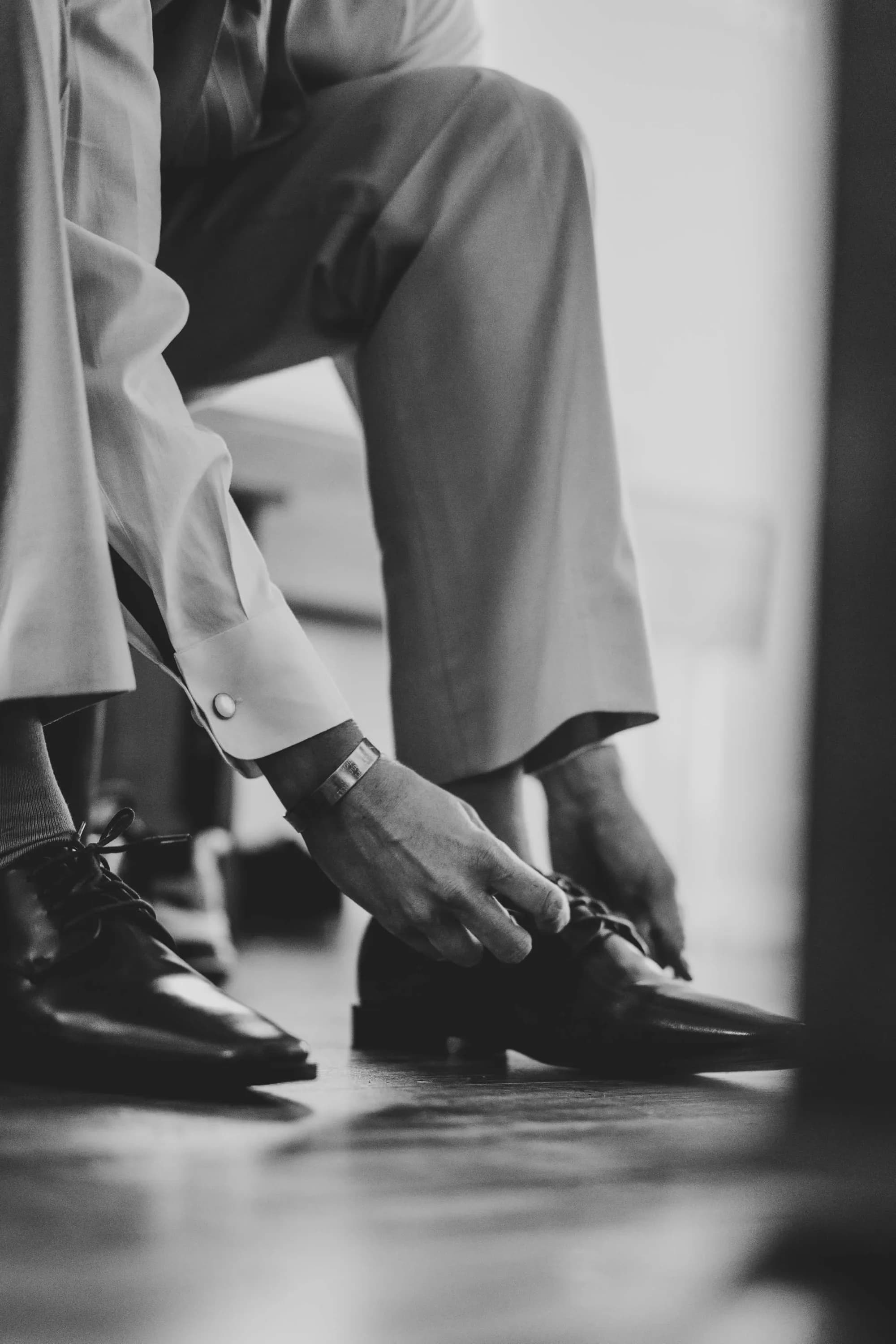 Black and white detail shot of groom's dress shoes and cufflinks with suit jacket