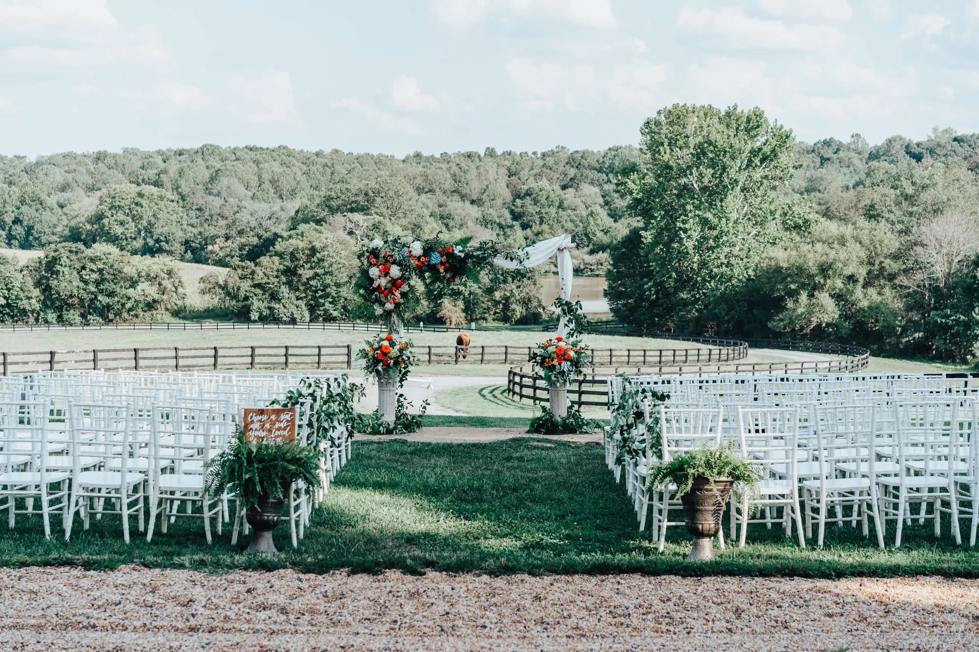 Outdoor wedding ceremony setup with white chairs, floral arch, and rolling Virginia countryside at Rixey Manor
