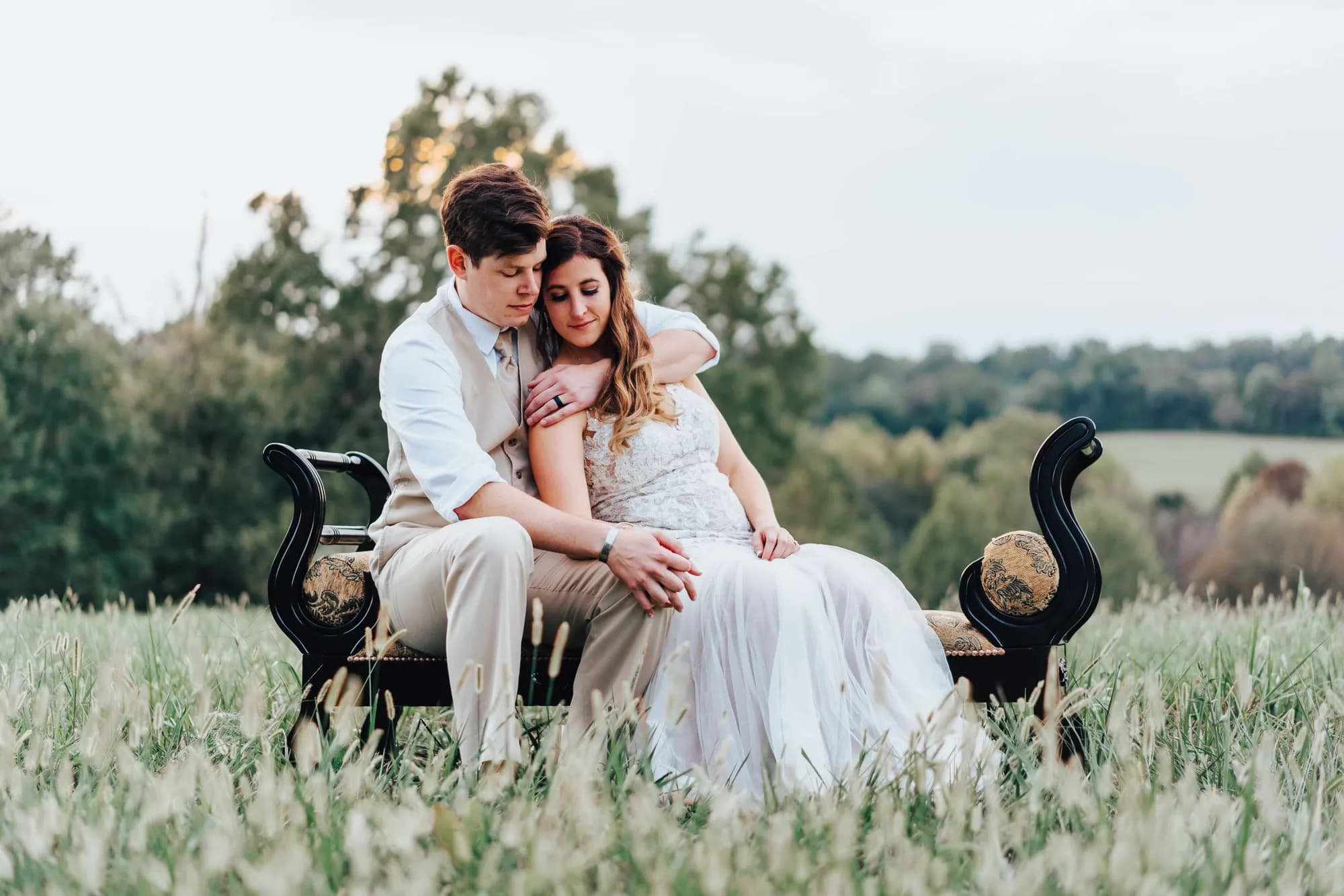 Bride and groom share a tender embrace on a vintage settee in Rixey Manor's sweeping meadow grounds at golden hour