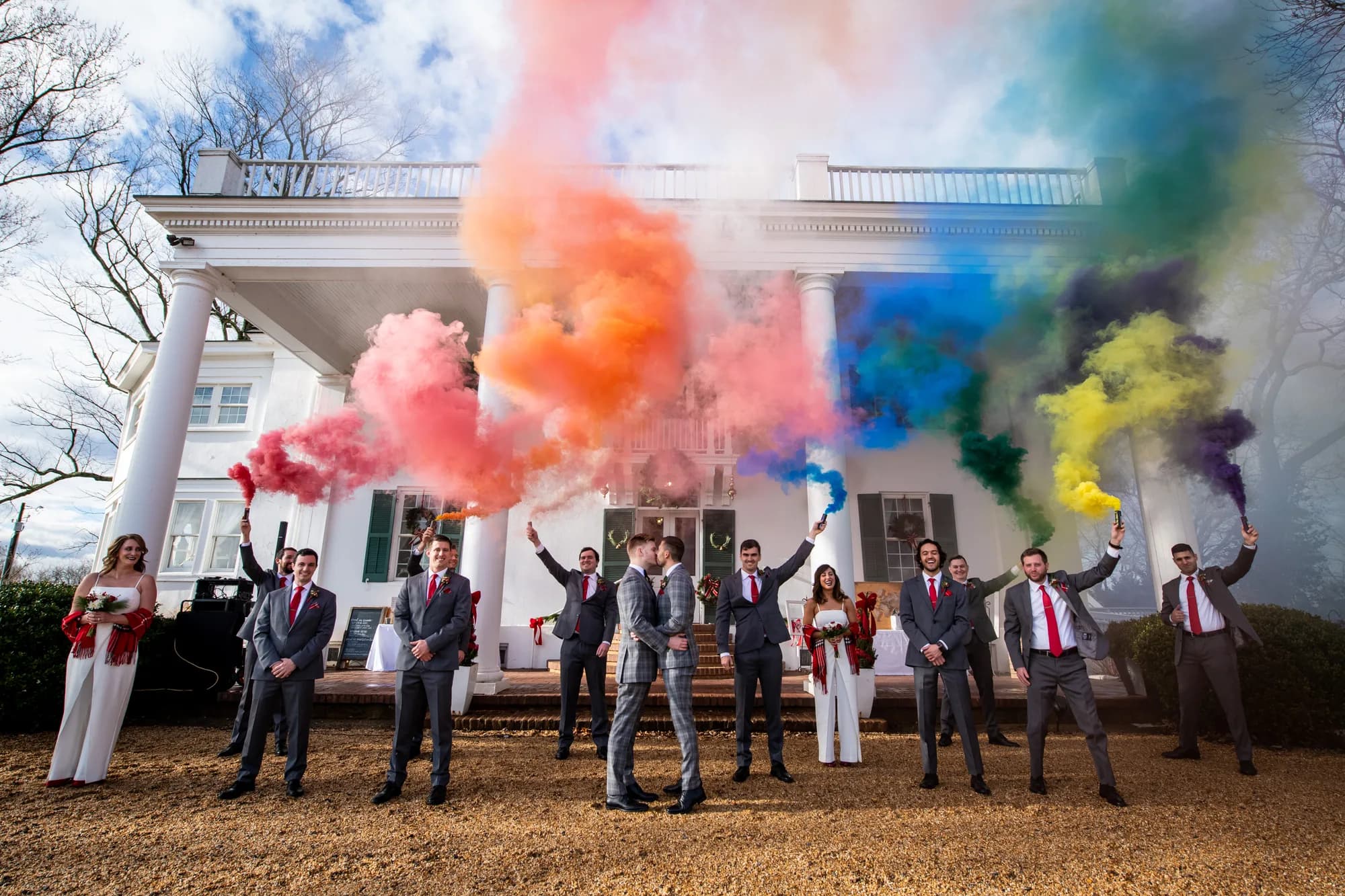 Two grooms kiss as wedding party releases rainbow smoke bombs outside Rixey Manor's white-columned facade