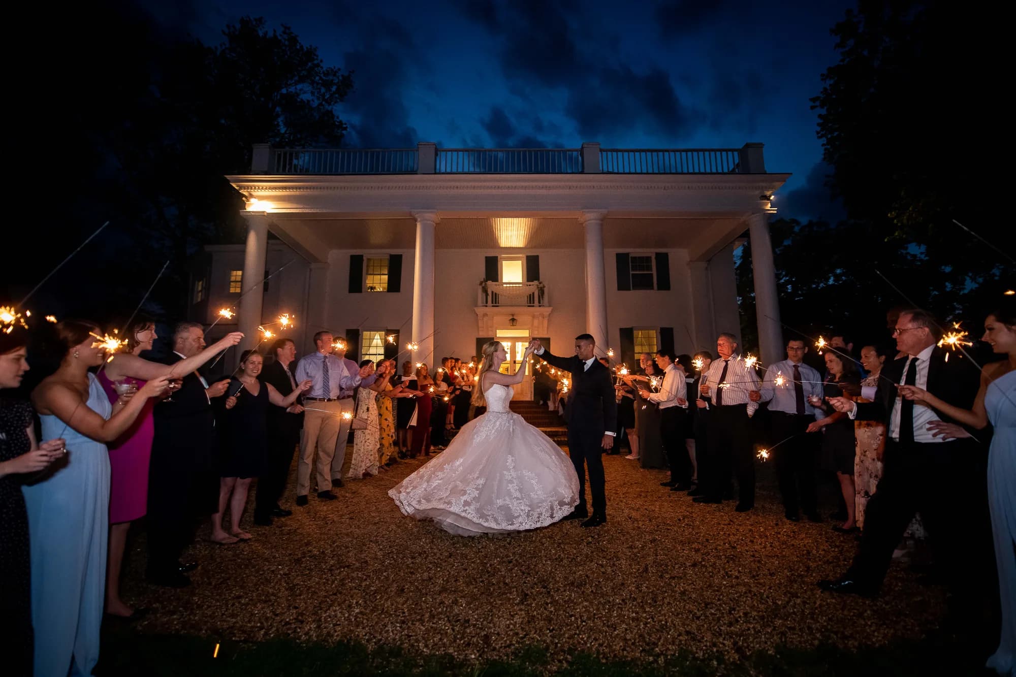 Bride and groom sparkler exit at night in front of Rixey Manor's illuminated white-columned facade