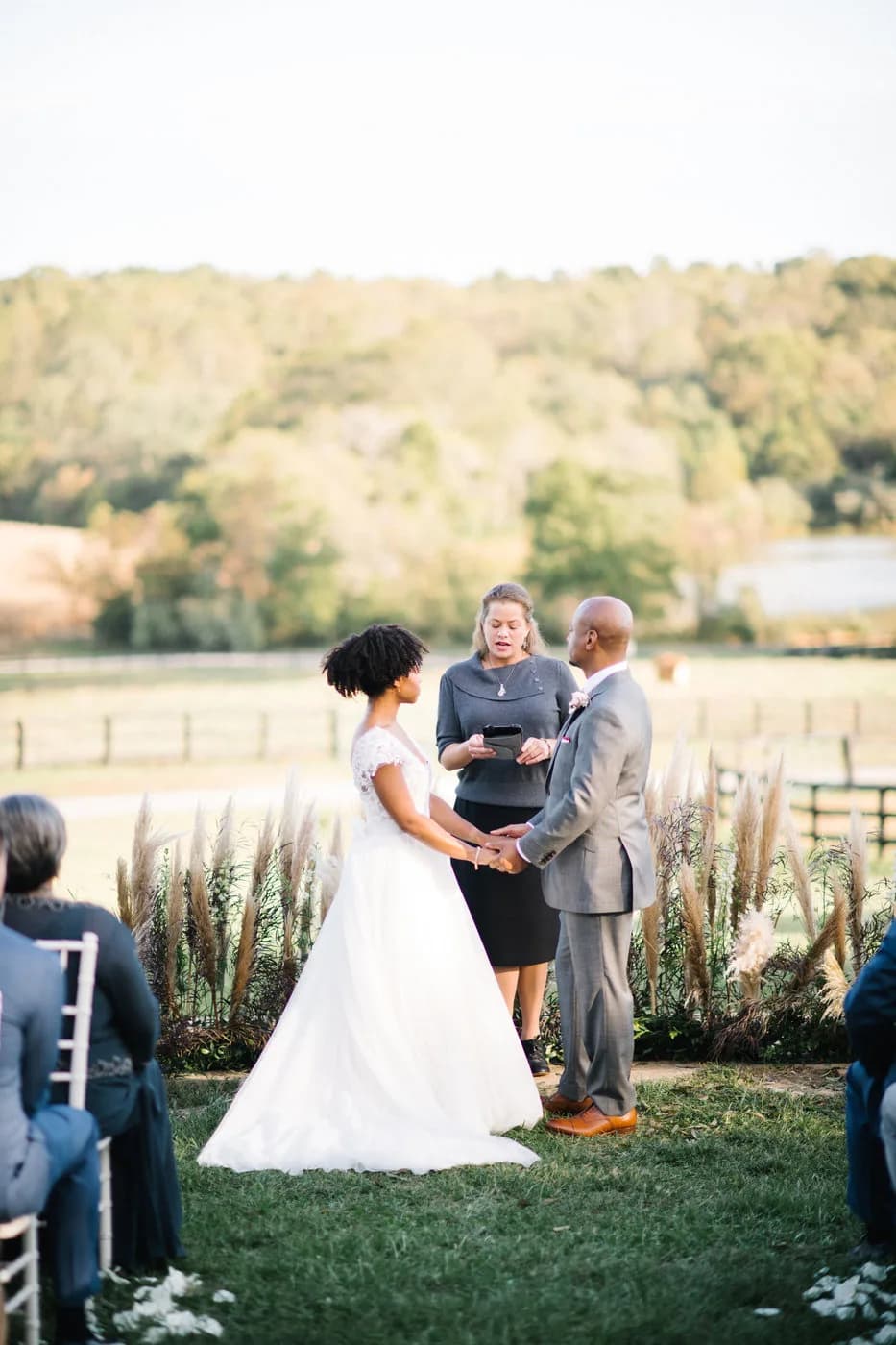Couple holds hands during outdoor ceremony at Rixey Manor with pastoral Virginia countryside backdrop