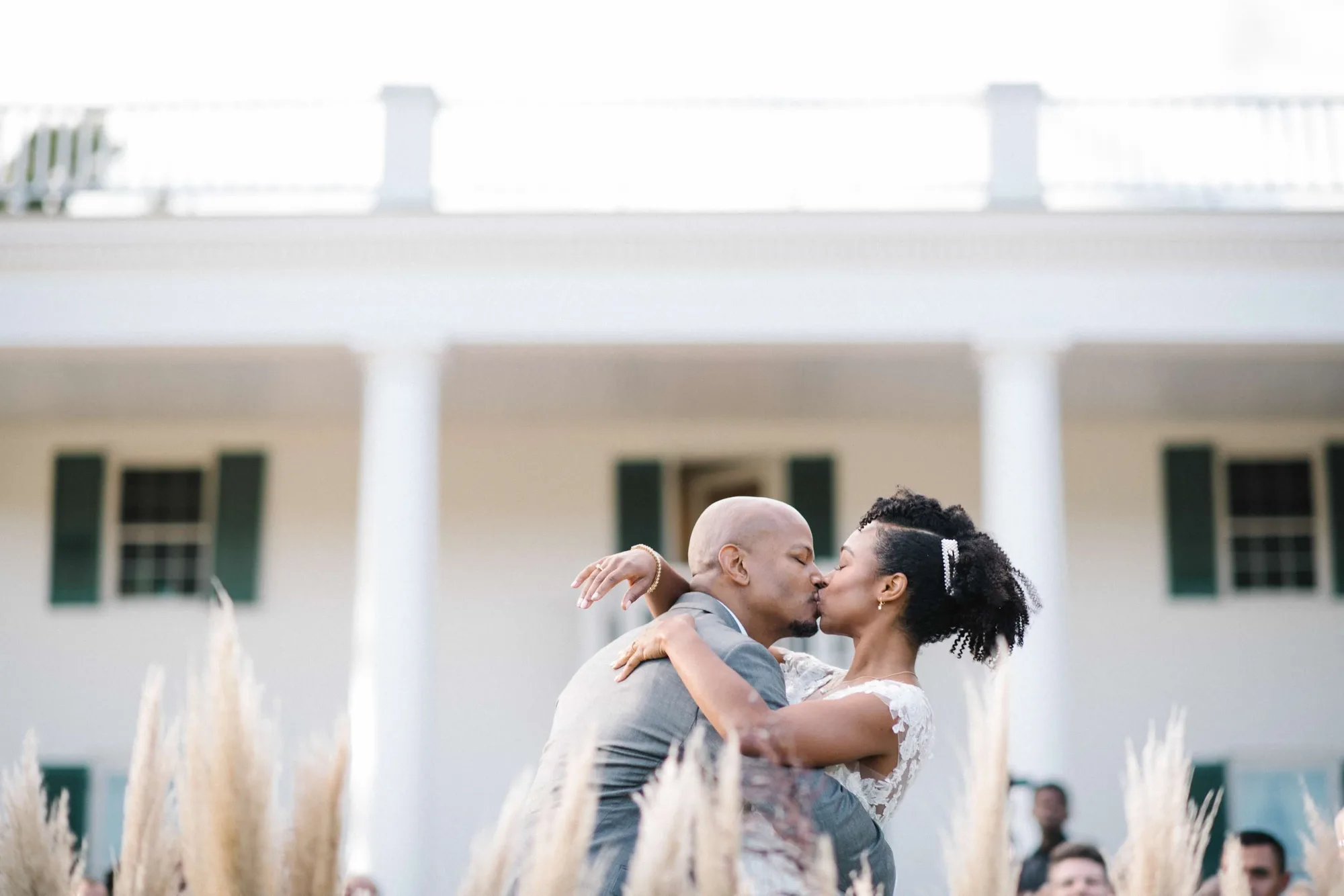 Couple shares first kiss in front of Rixey Manor's white columned facade amid tall pampas grass
