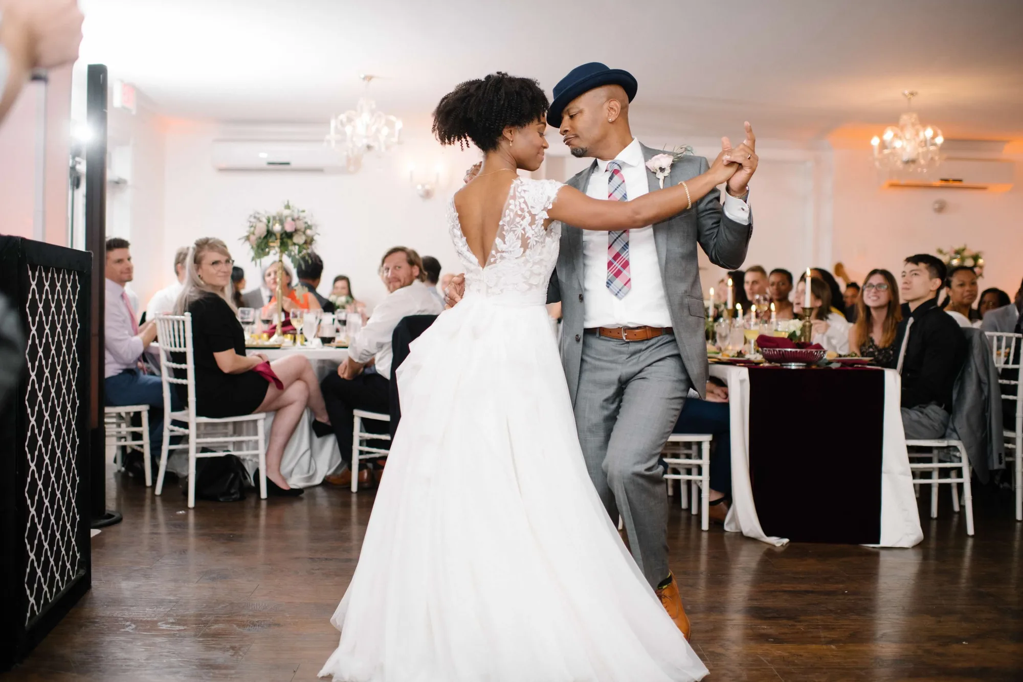 Bride and groom share first dance in chandelier-lit ballroom as wedding guests look on