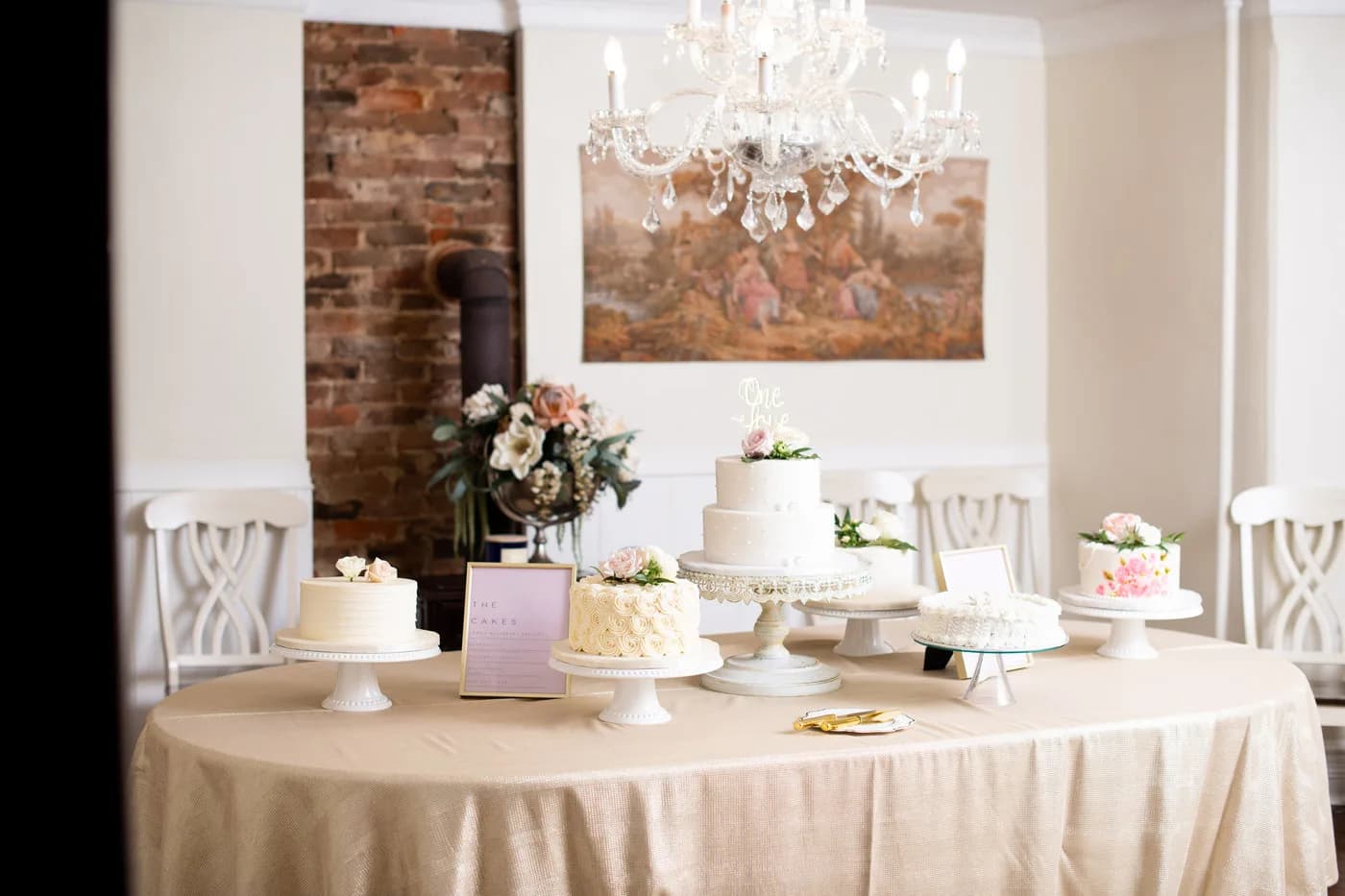 Wedding cake display table with multiple white tiered cakes under a crystal chandelier at Rixey Manor
