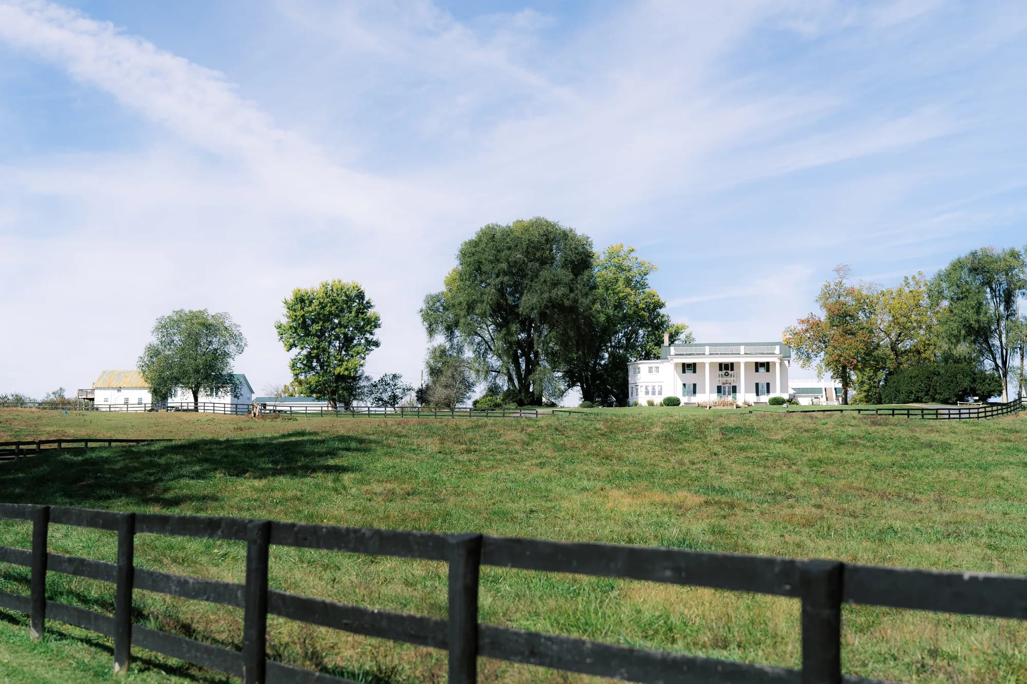 Wide view of Rixey Manor estate across green pastures with black wood fencing on a clear autumn day.