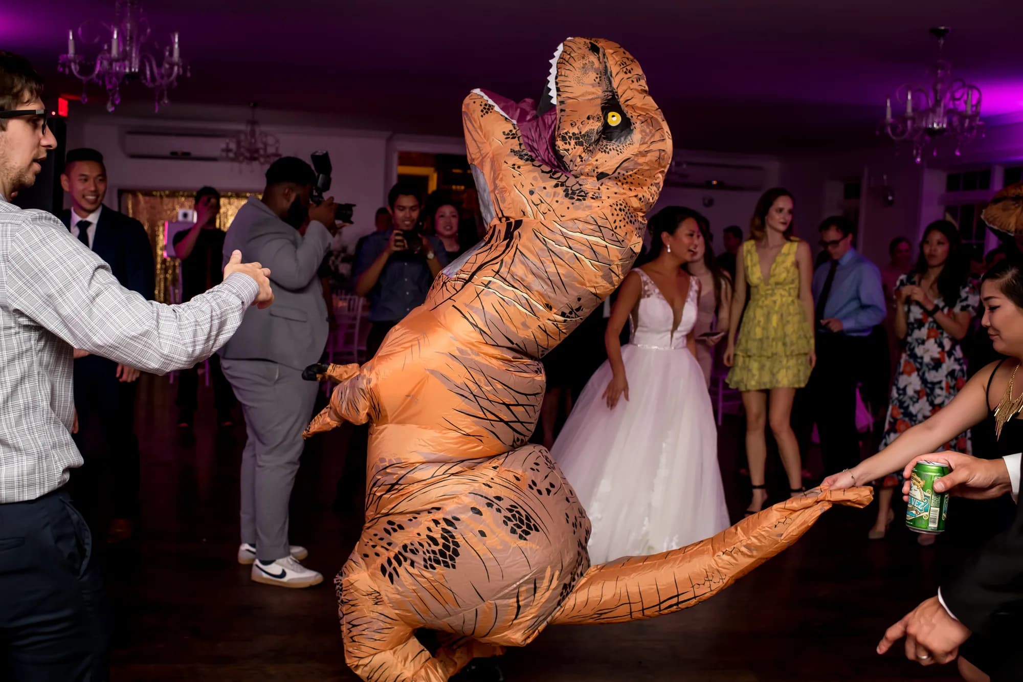 Guest in inflatable T-Rex costume dancing at wedding reception with guests watching and laughing