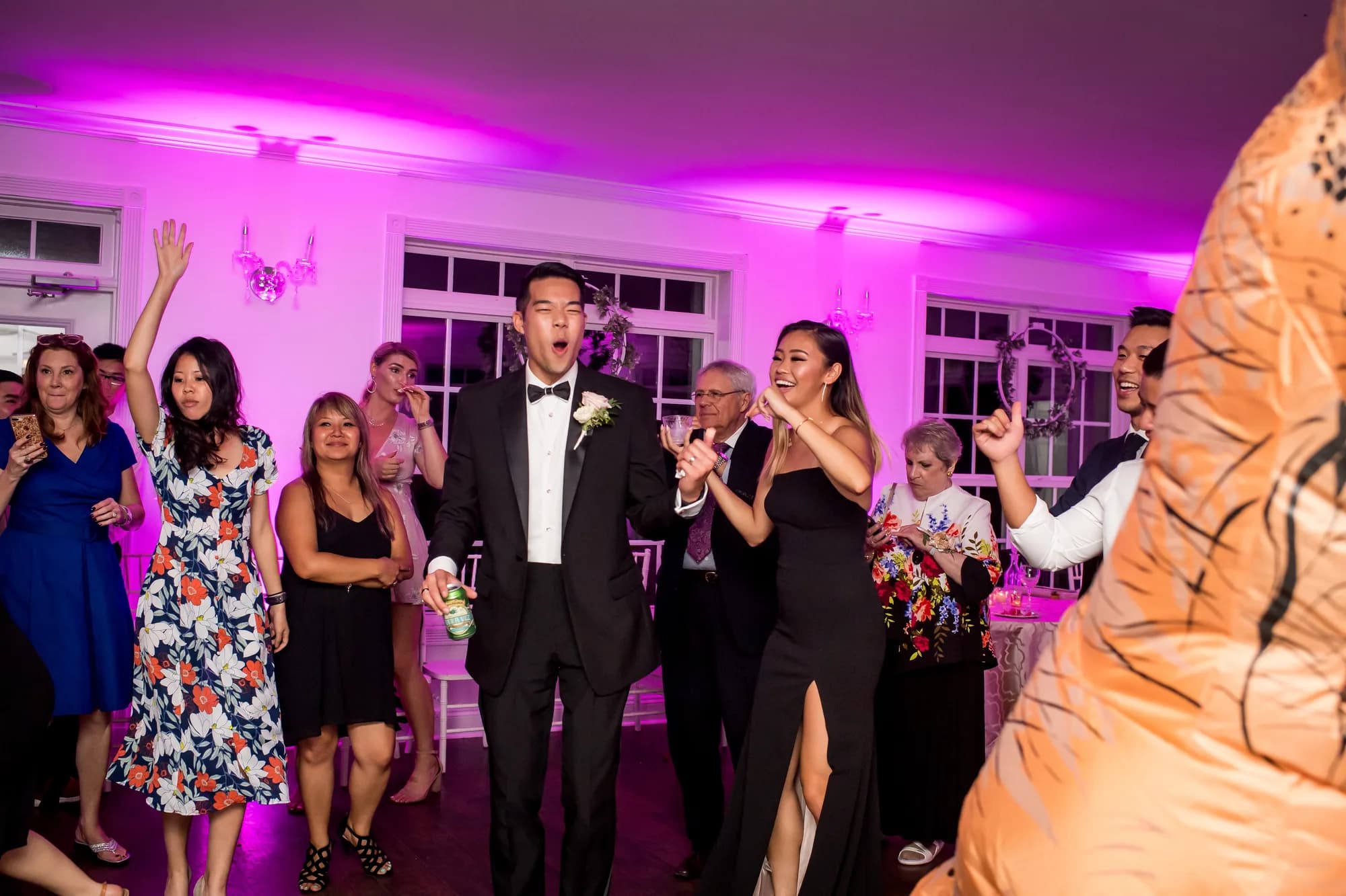 Groom singing and celebrating on the dance floor surrounded by joyful wedding guests under pink uplighting