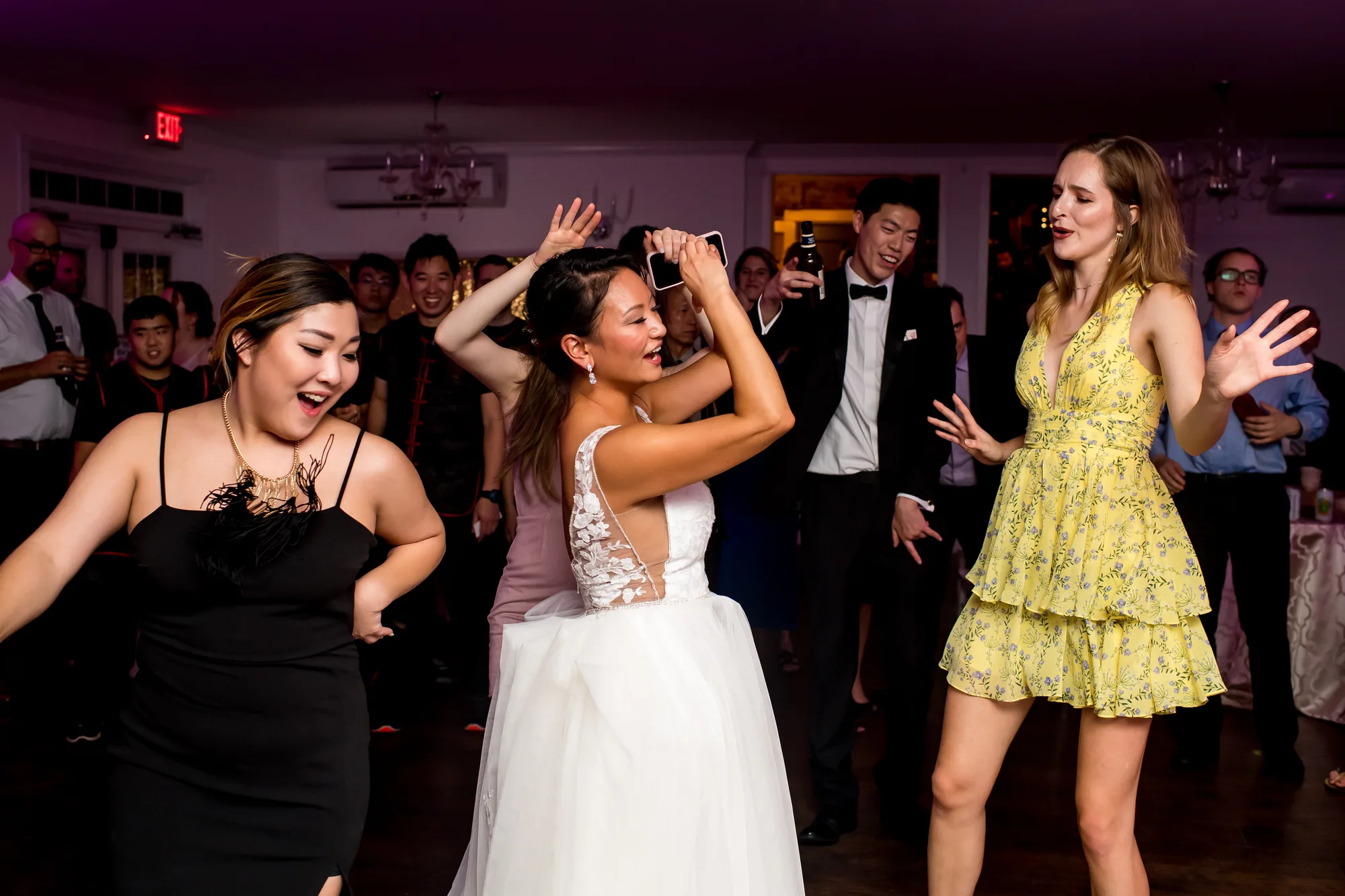 Bride dancing joyfully with guests on the reception dance floor, surrounded by smiling friends in evening attire.