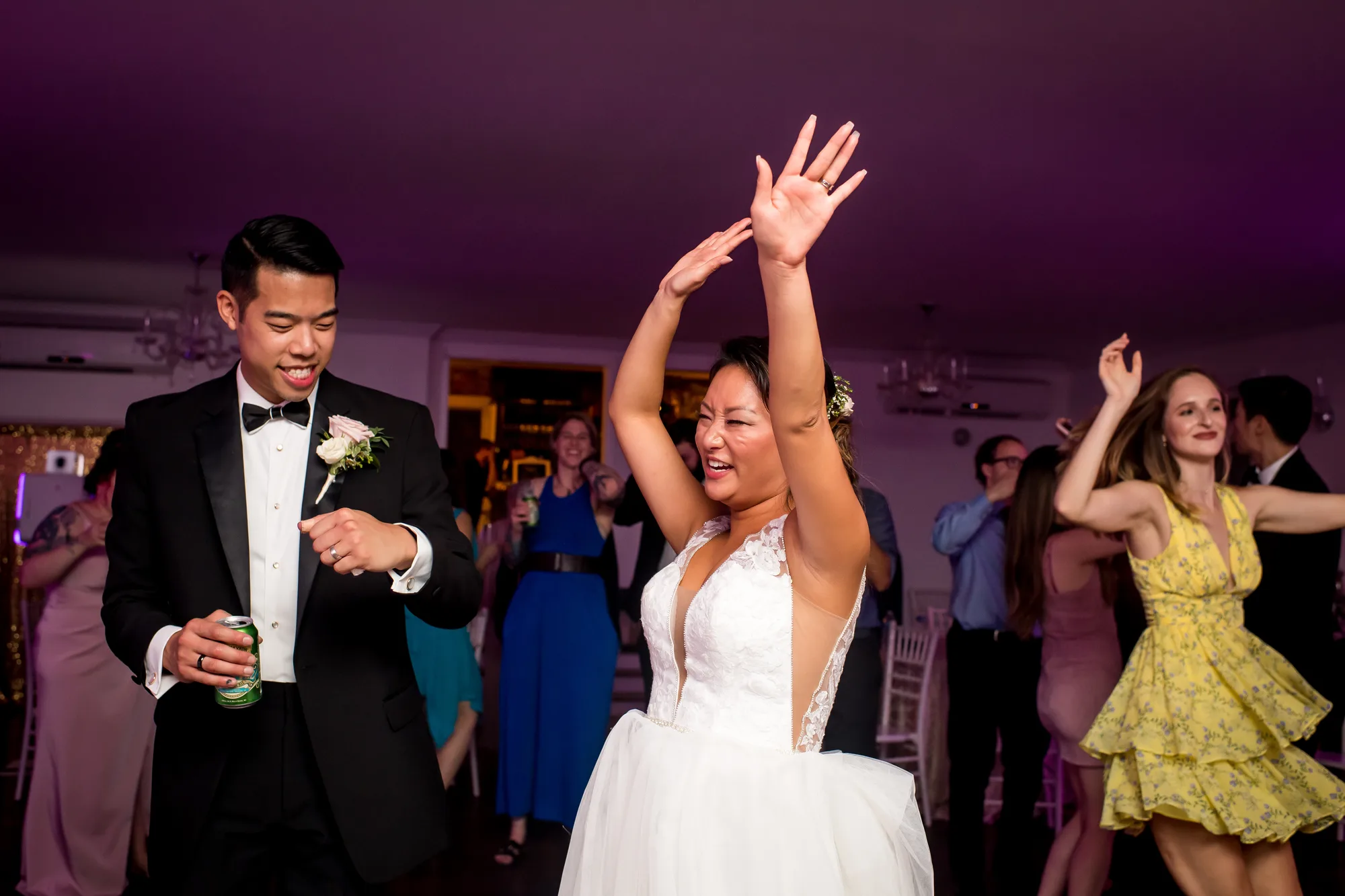Bride raises arms joyfully on the dance floor beside her groom during wedding reception celebration