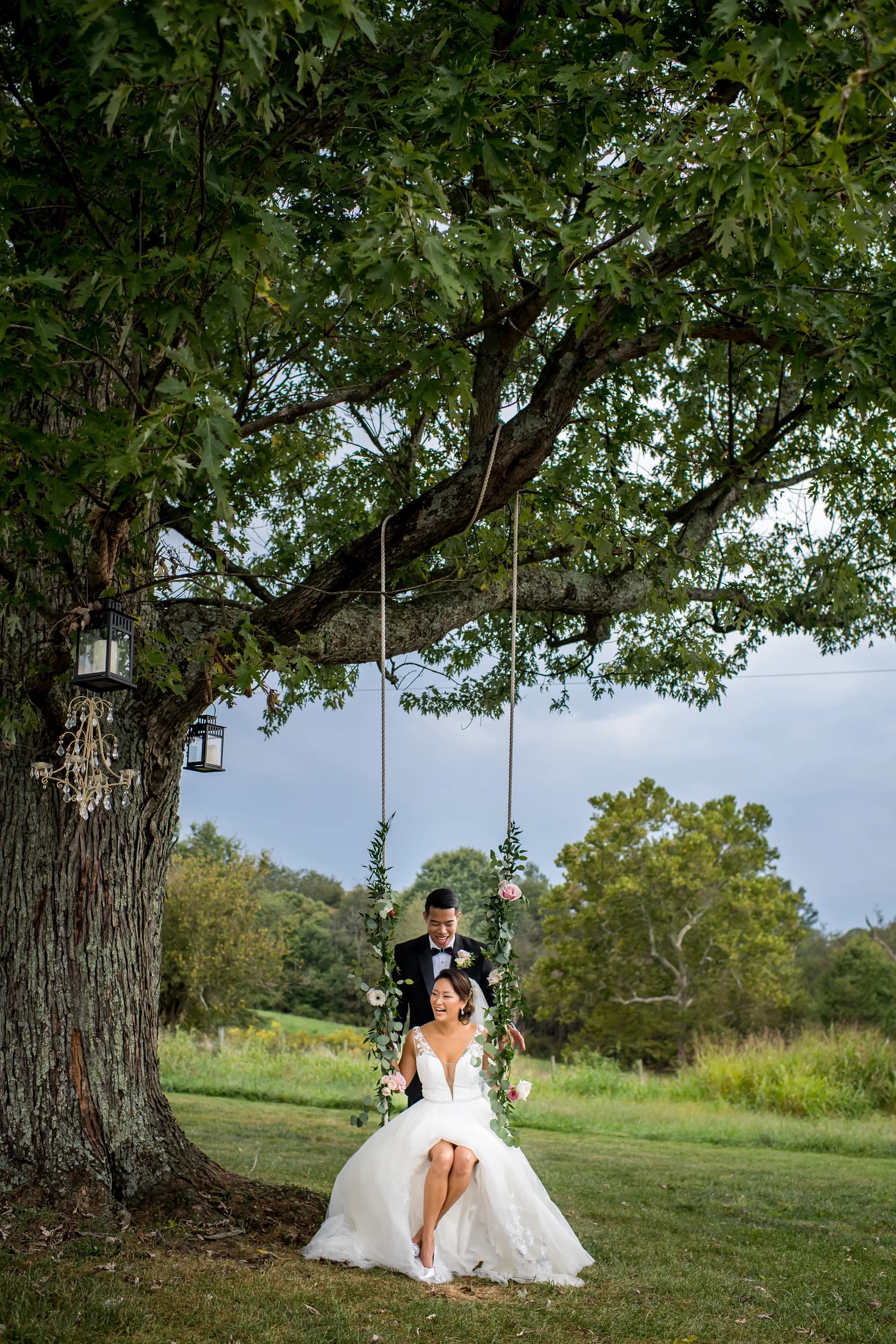 Bride and groom on a flower-draped tree swing beneath a grand oak on Rixey Manor's lush green grounds