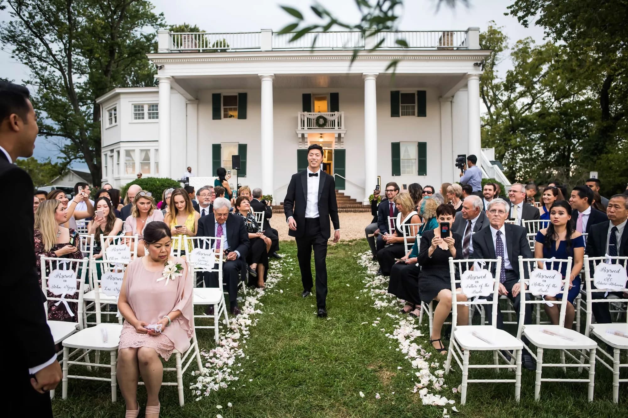 Groom walks down the aisle at Rixey Manor outdoor ceremony with white colonial mansion backdrop
