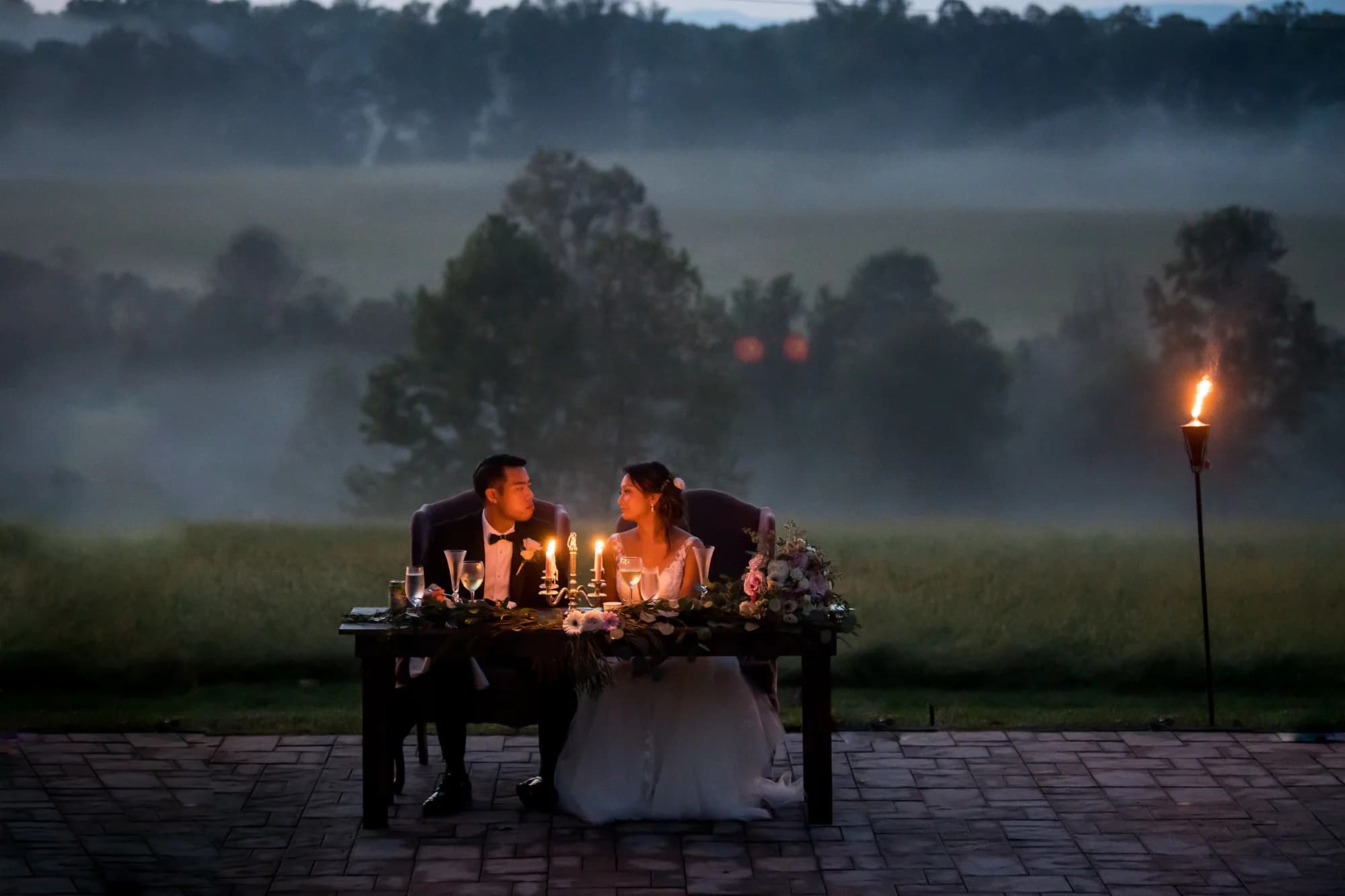Bride and groom share a candlelit sweetheart table at dusk overlooking Rixey Manor's misty Virginia countryside